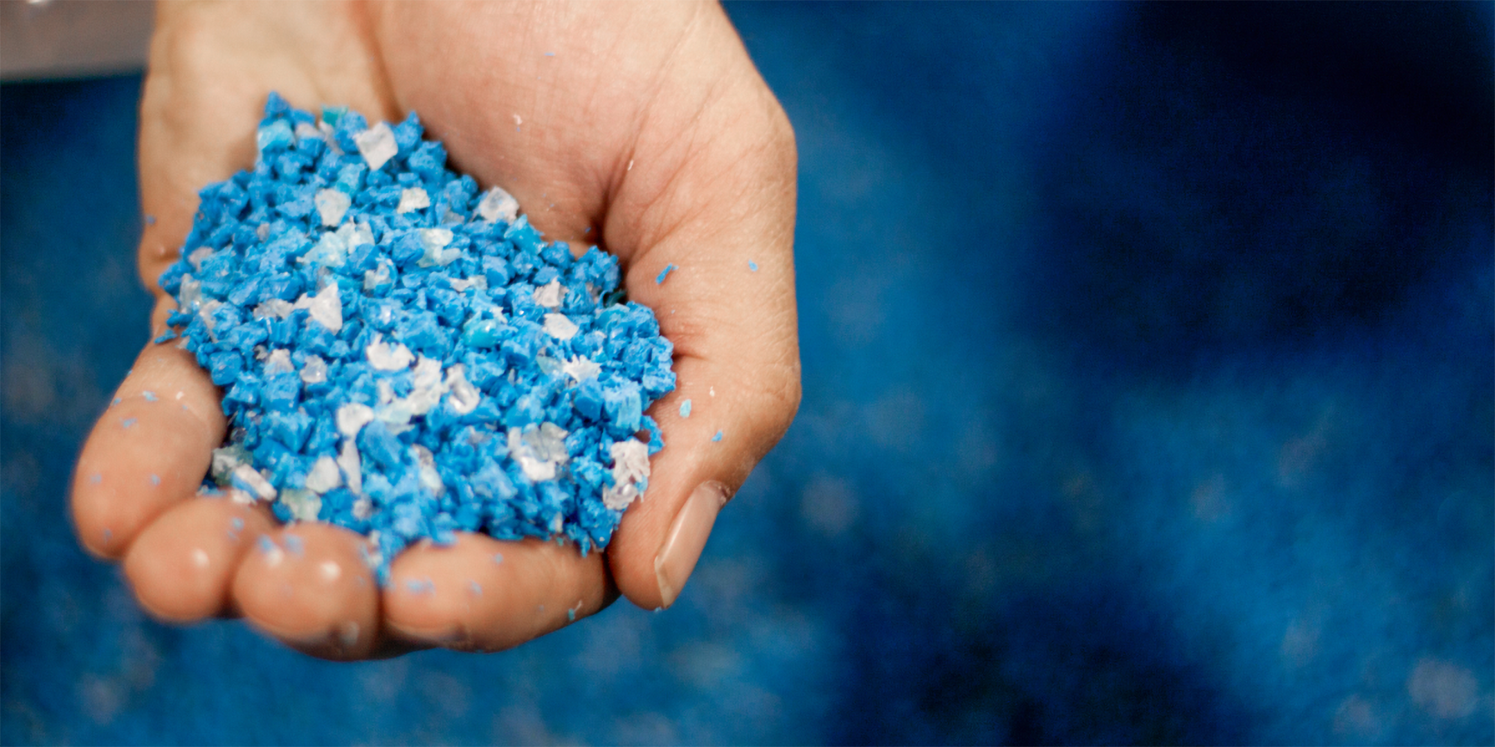 Eine Hand voller blauem und weißem recycletem Kunststoffgranulat.