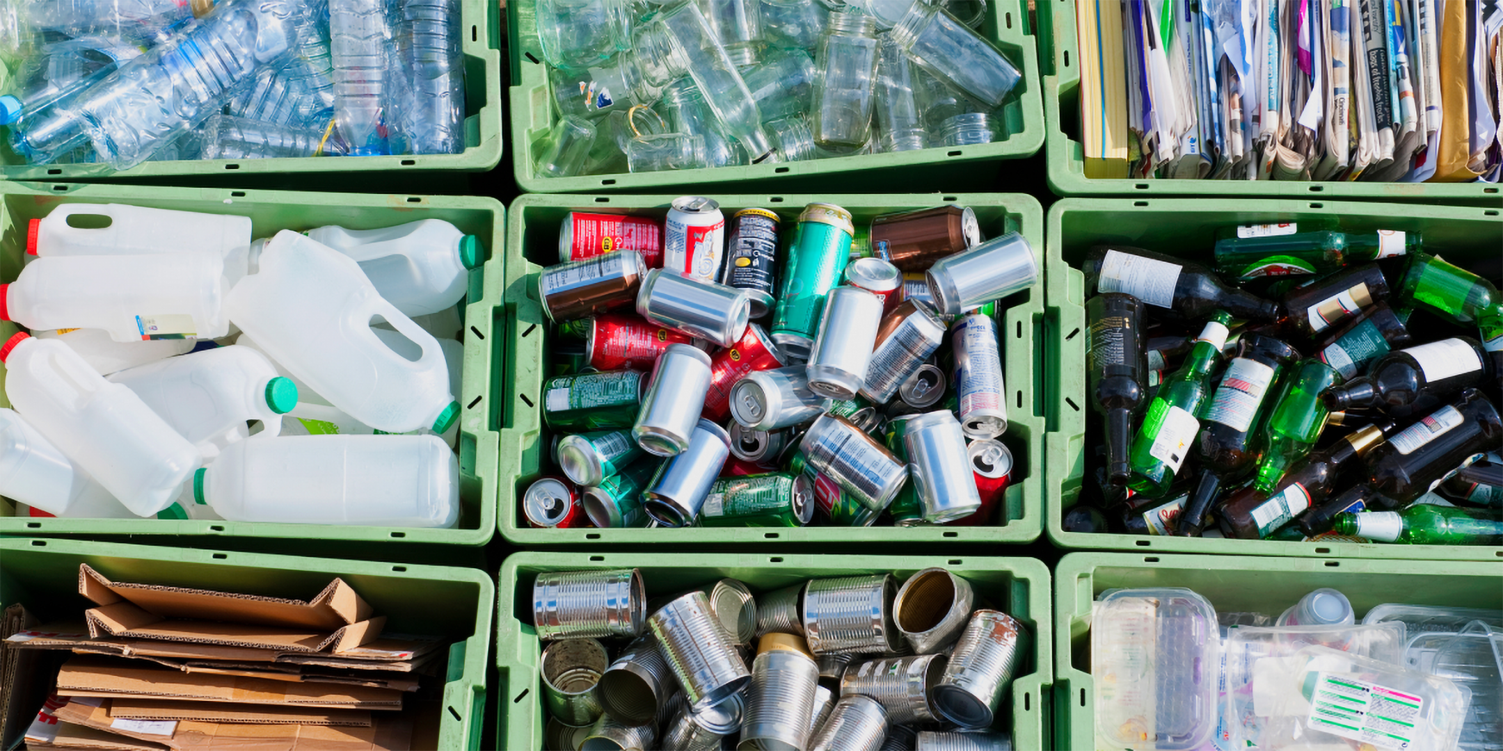 Boxen gefüllt mit recyclebaren Verpackungenen wie Getränkedosen und Glasflaschen.