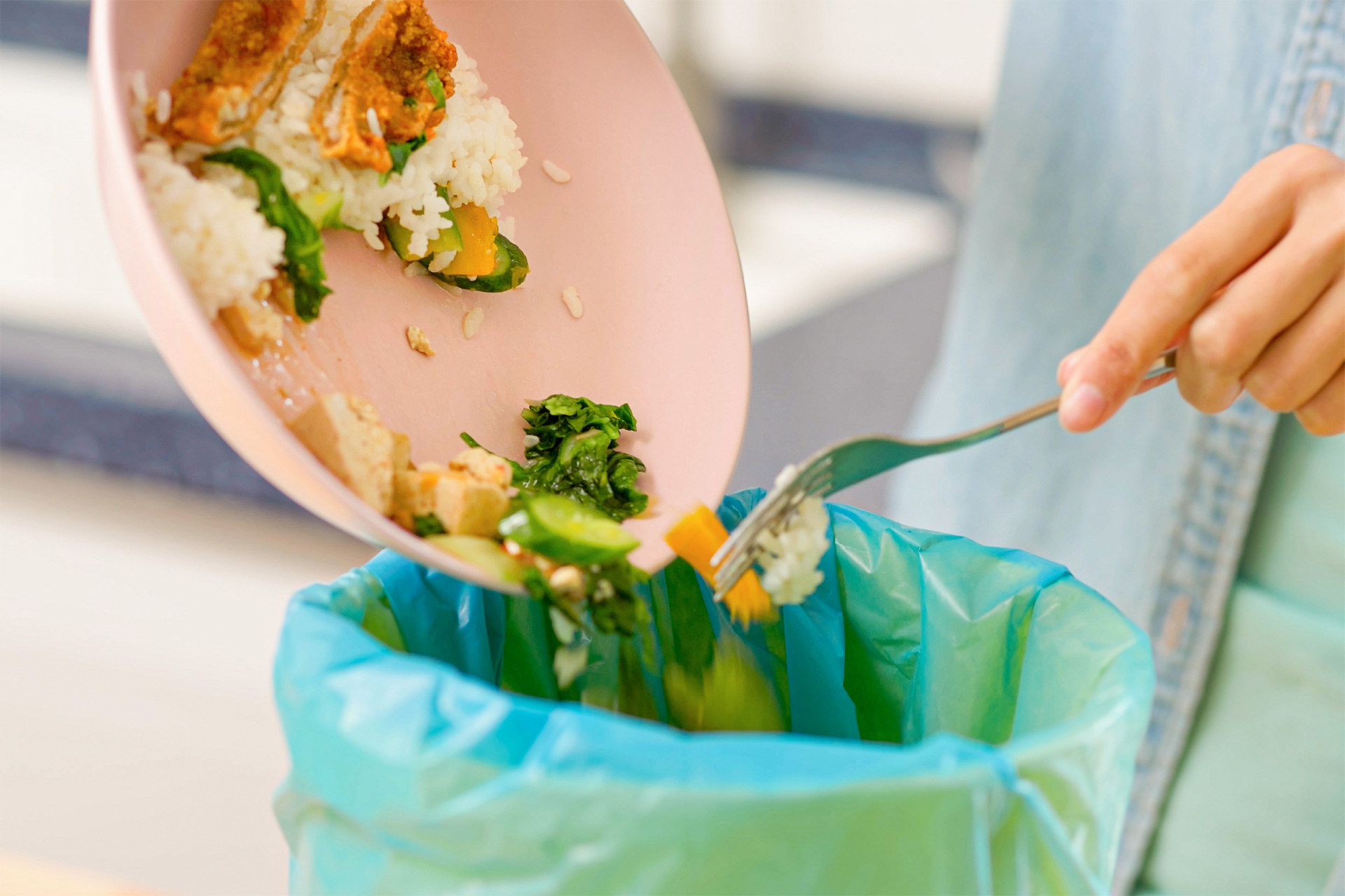 Eine Person ist gerade dabei größere Essensreste von Ihrem Teller in den Mülleimer zu leeren.