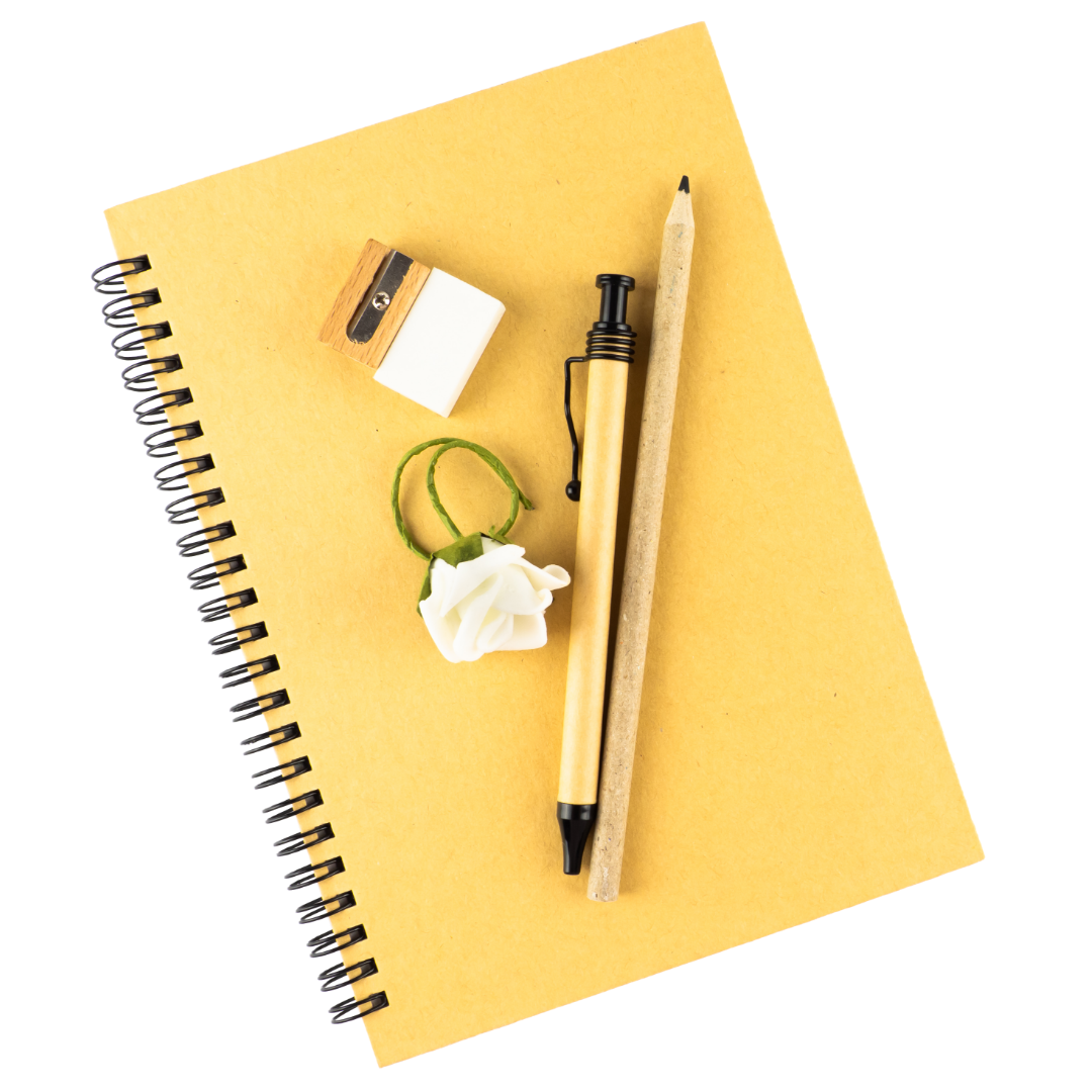Gelbes Notizbuch, auf dem ein Bleistift, ein Kugelschreiber und ein Anspitzer liegen.