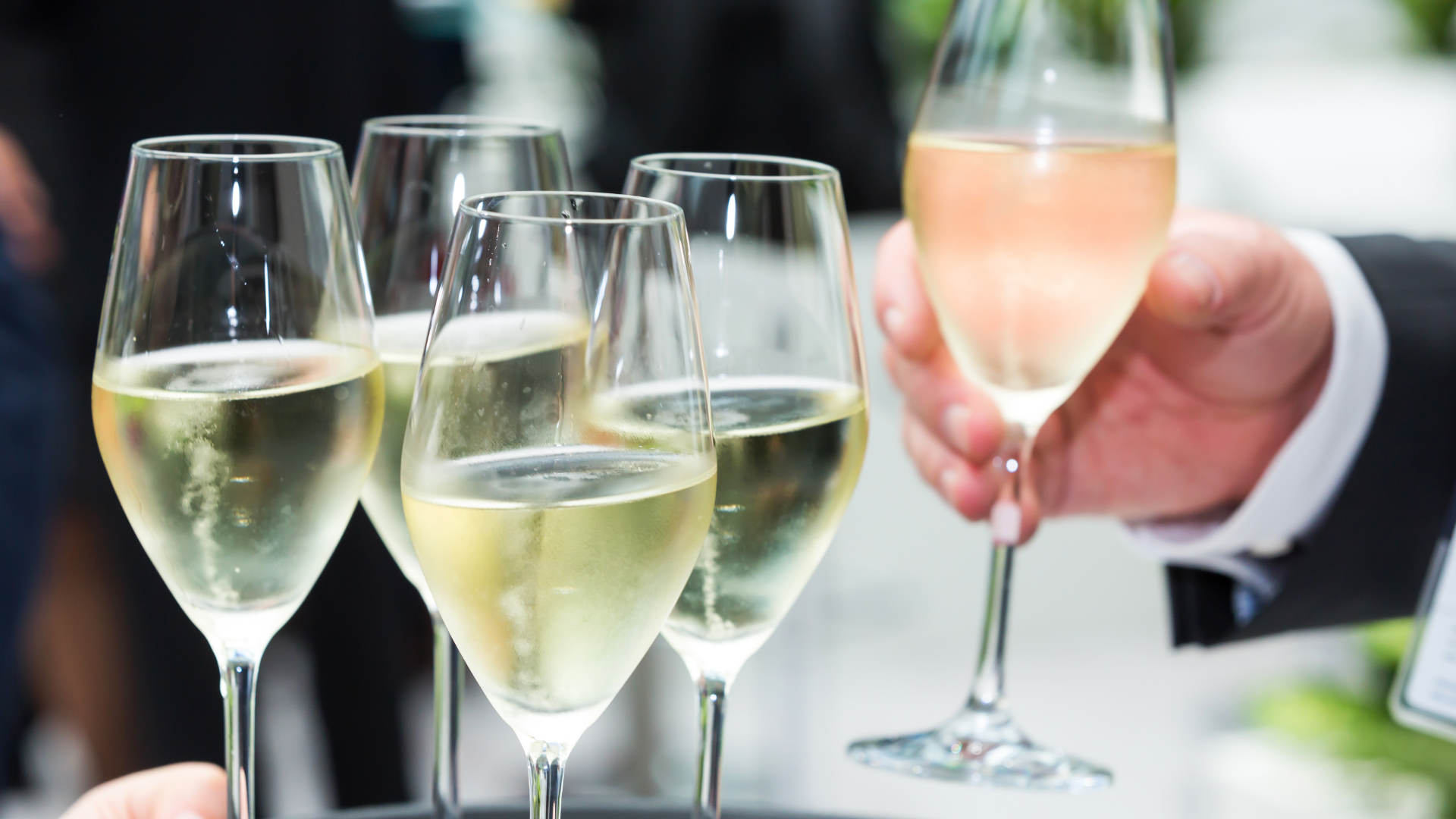 Serviertablett mit Sektgläsern, eines in der Hand.