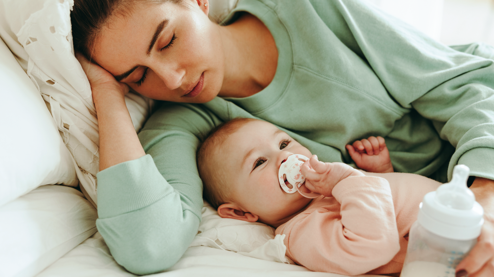 Mutter mit Baby und Flasche auf Bett.
