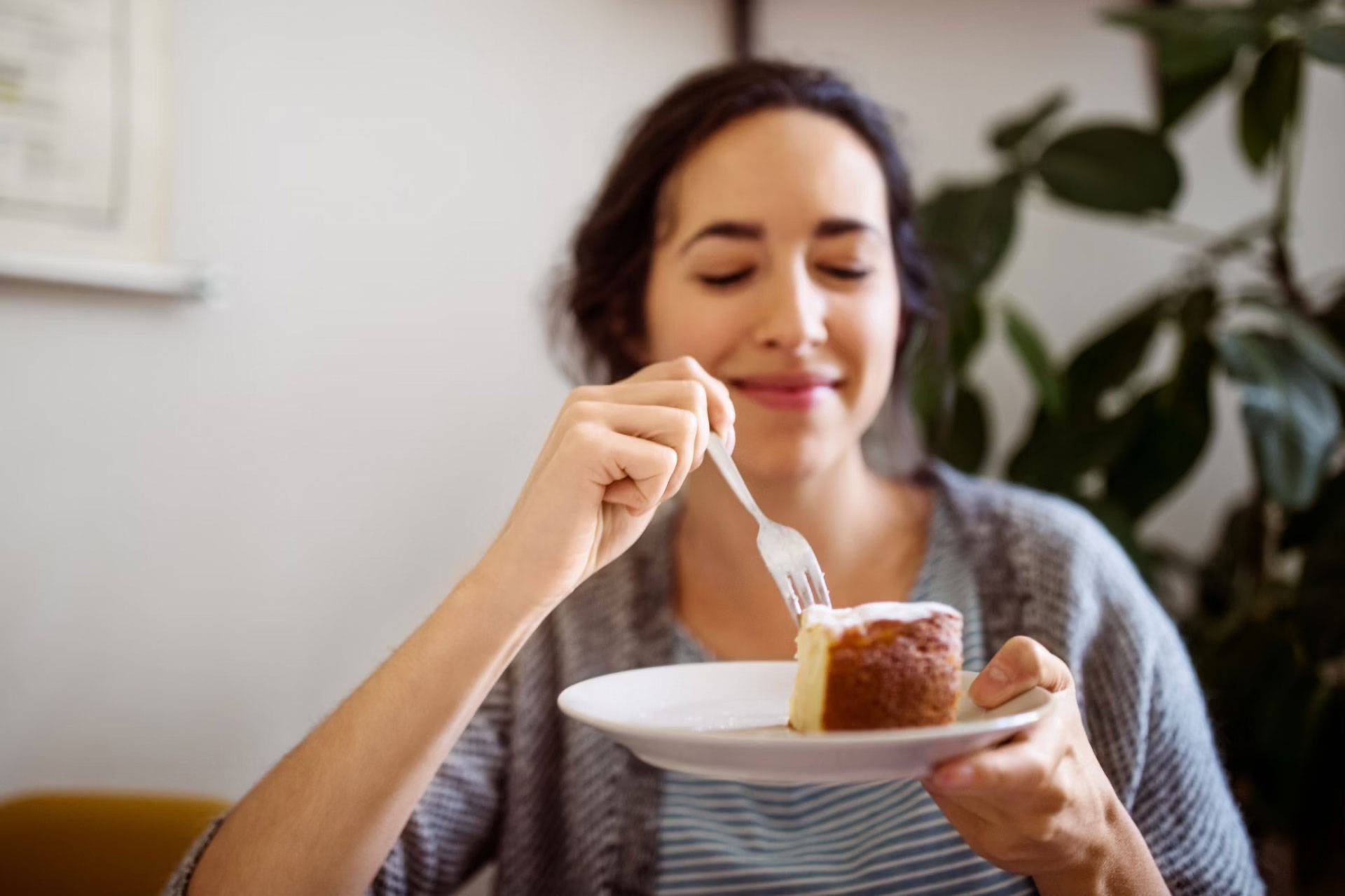 Frau genießt ein Stück Kuchen auf einem Teller mit einer Gabel.