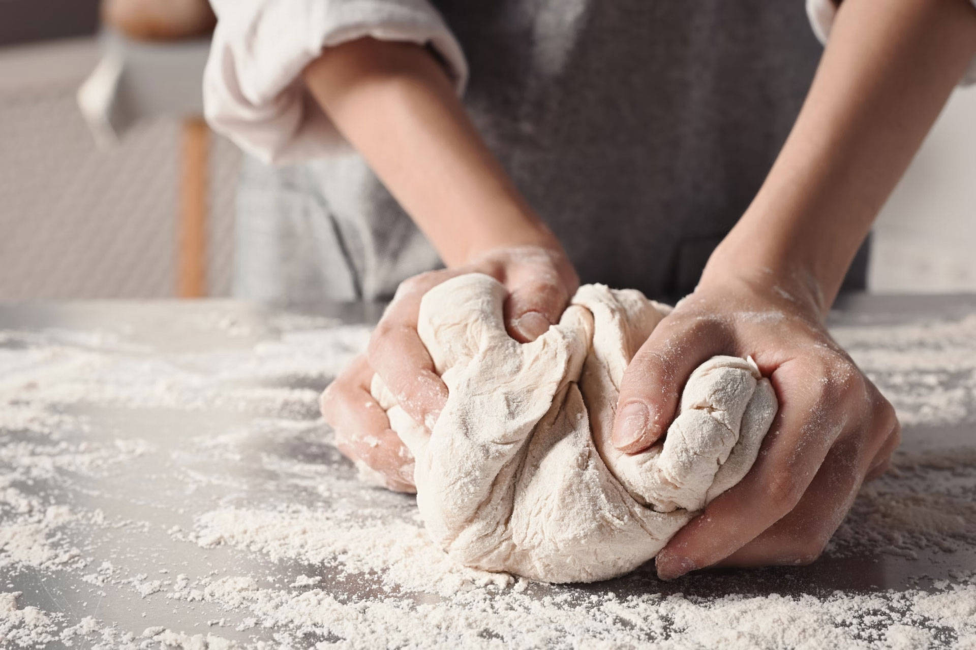 Jemand knetet Teig mit den Händen auf einer bemehlten Arbeitsfläche.