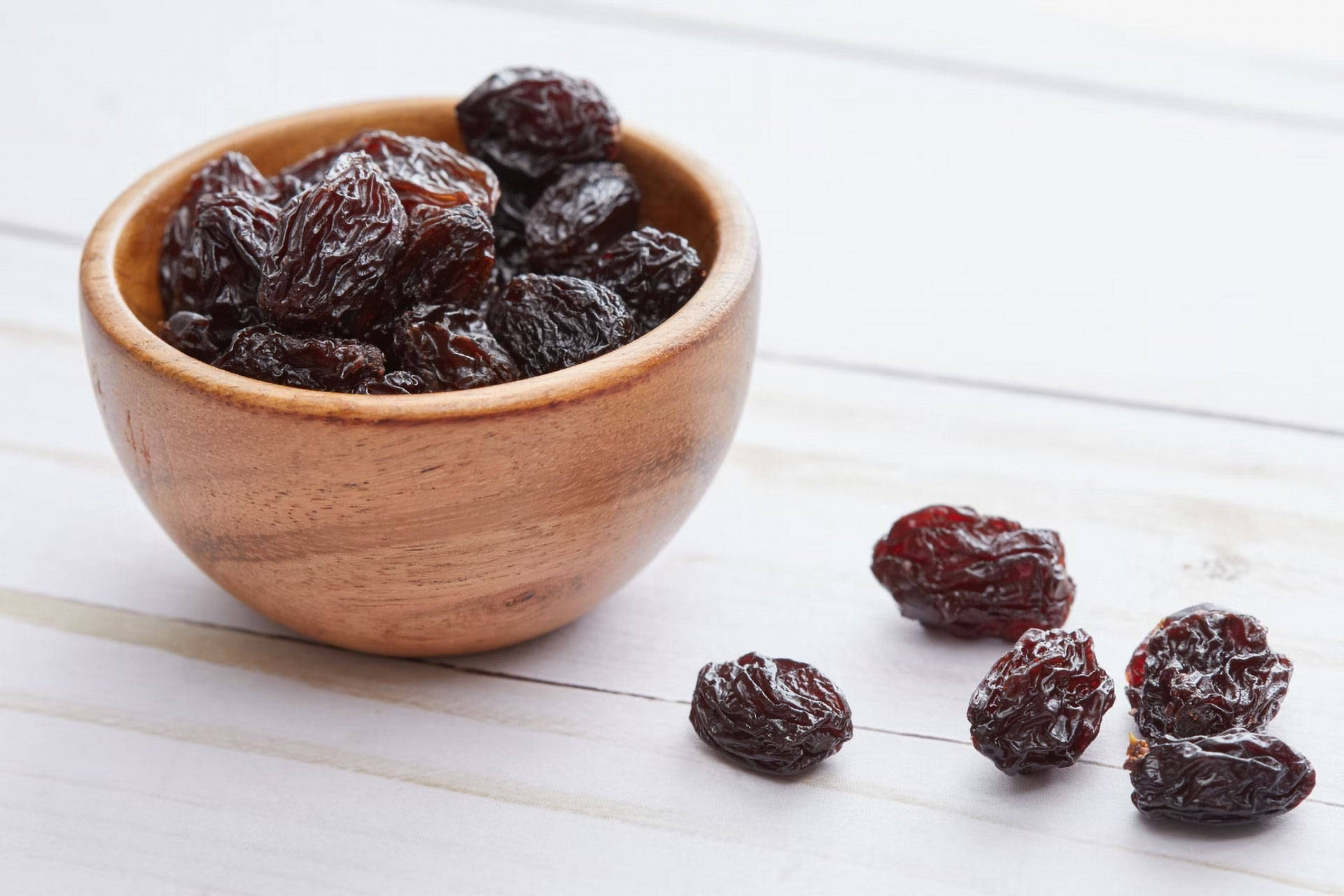 Holzschale gefüllt mit dunklen Rosinen, einige daneben liegend.