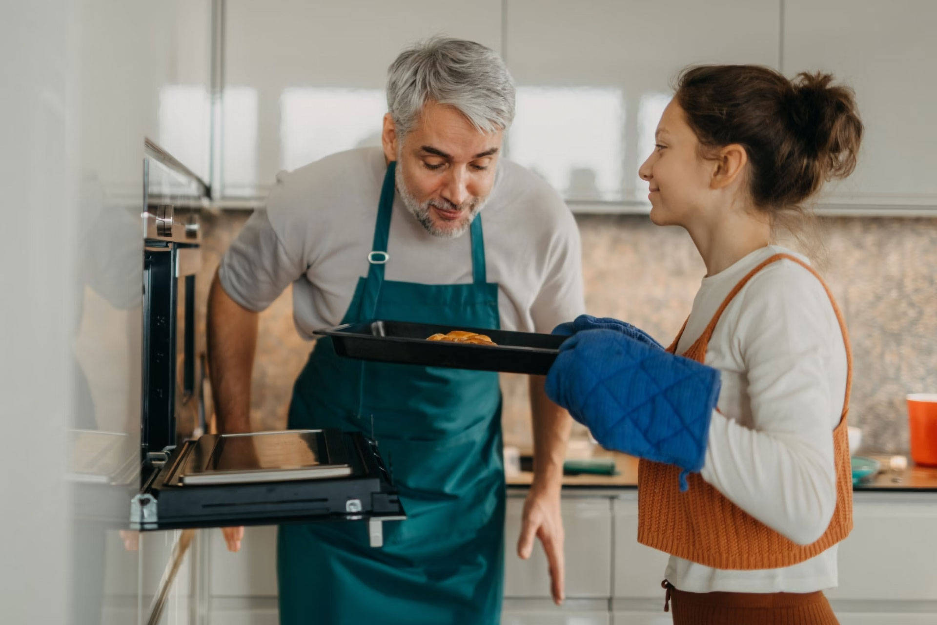 Vater und Tochter prüfen gebackenes Gericht auf einem Ofenblech.