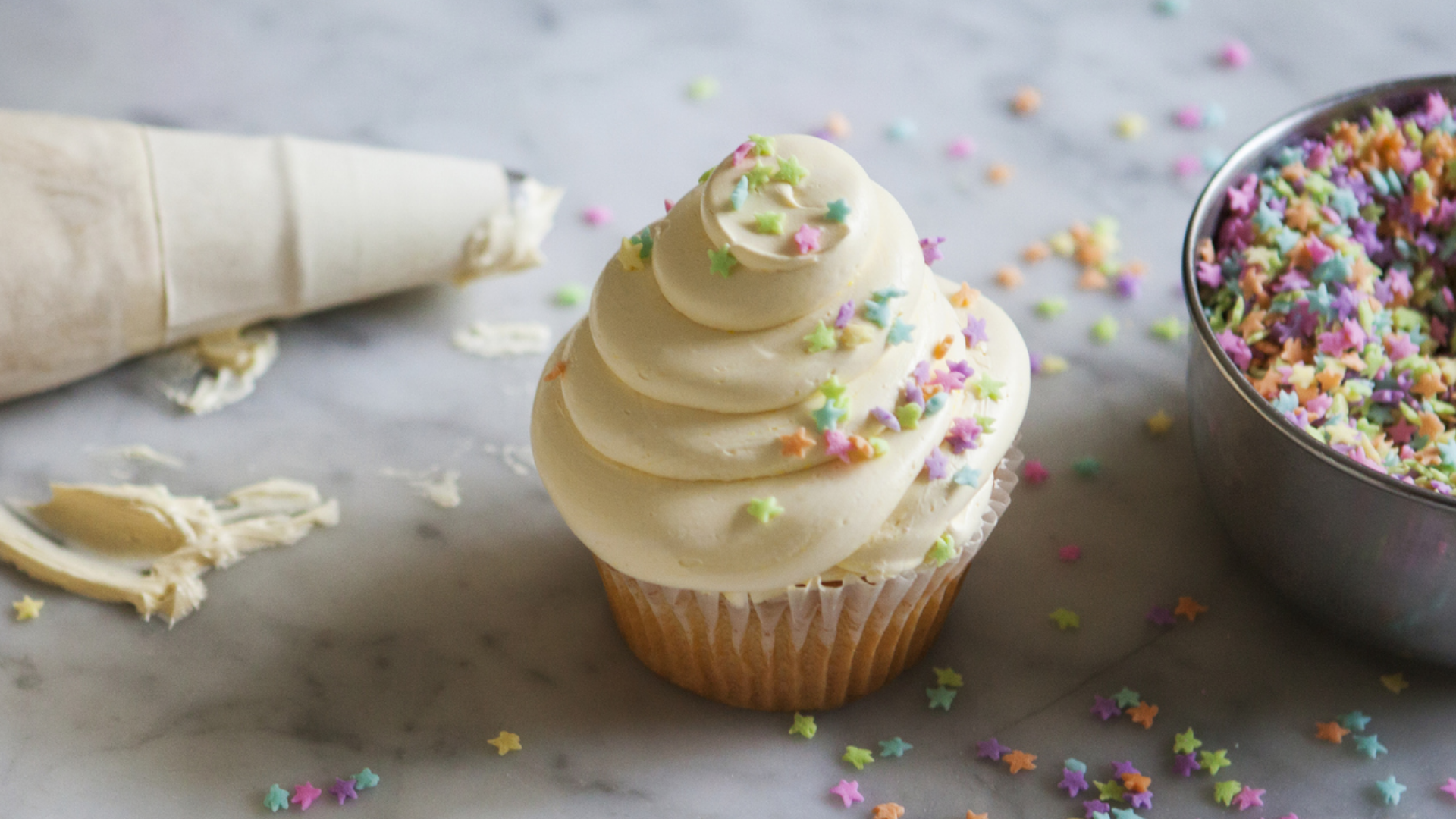 Verzierter Cupcake mit Spritzbeutel und Sternchenstreusel.