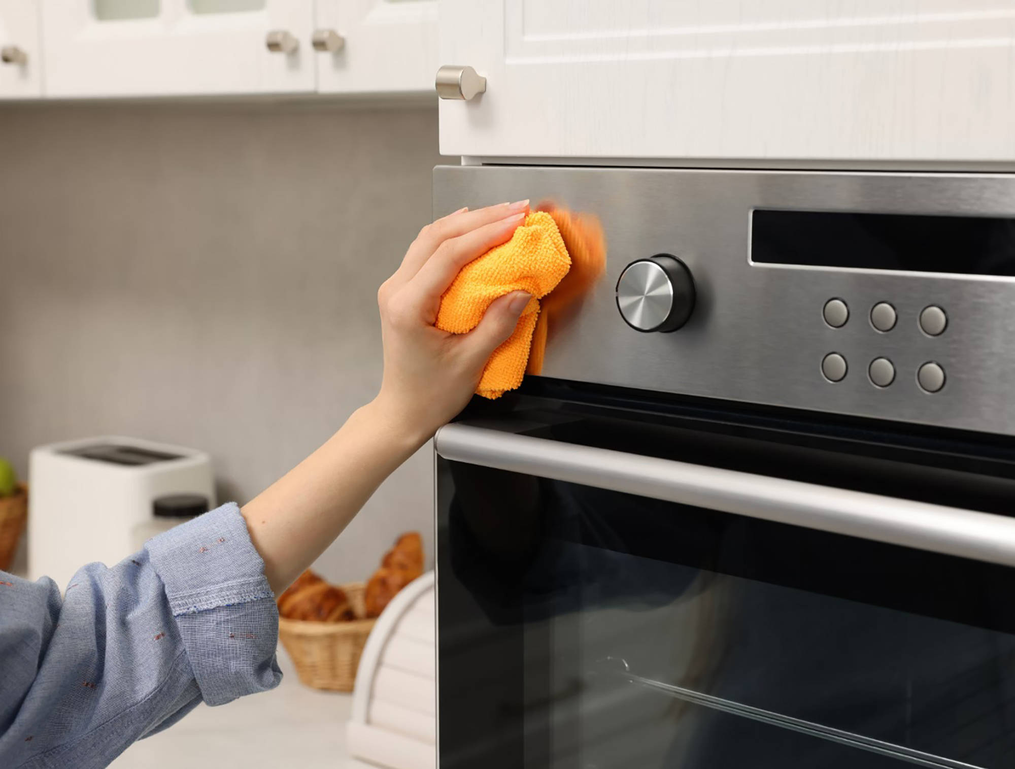 Person reinigt mit einem orangefarbenen Mikrofasertuch die Edelstahlfront eines Backofens.