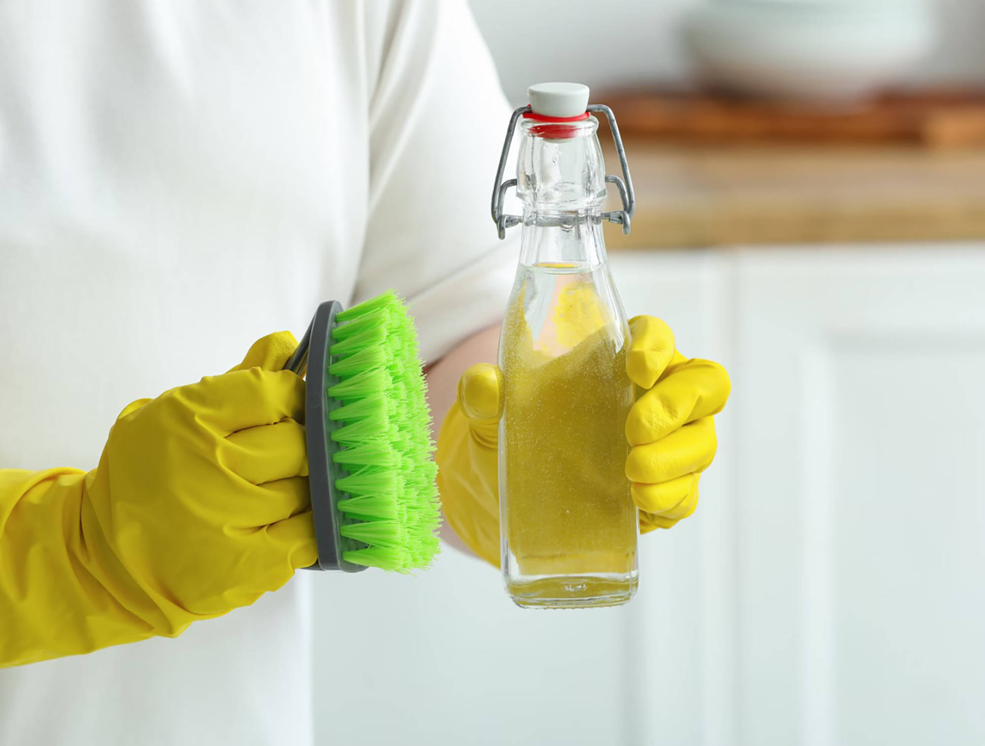 Person mit gelben Gummihandschuhen hält eine grüne Reinigungsbürste und eine Flasche mit selbstgemachtem natürlichem Rei