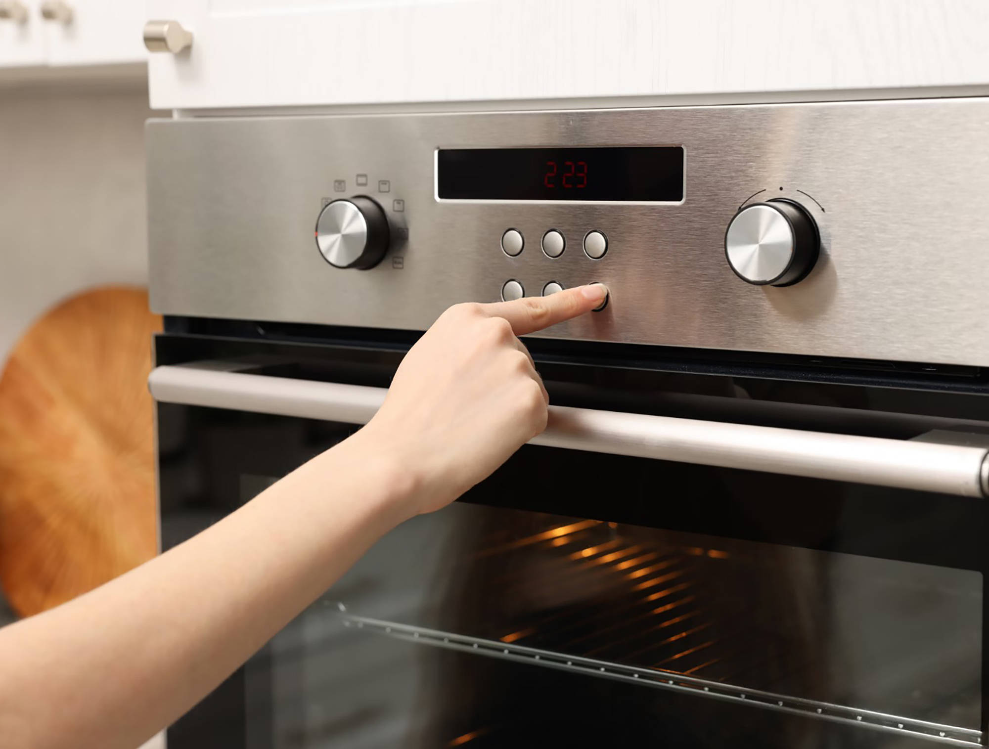 Person drückt die Taste eines modernen Edelstahl-Backofens mit digitaler Anzeige in einer Küche.