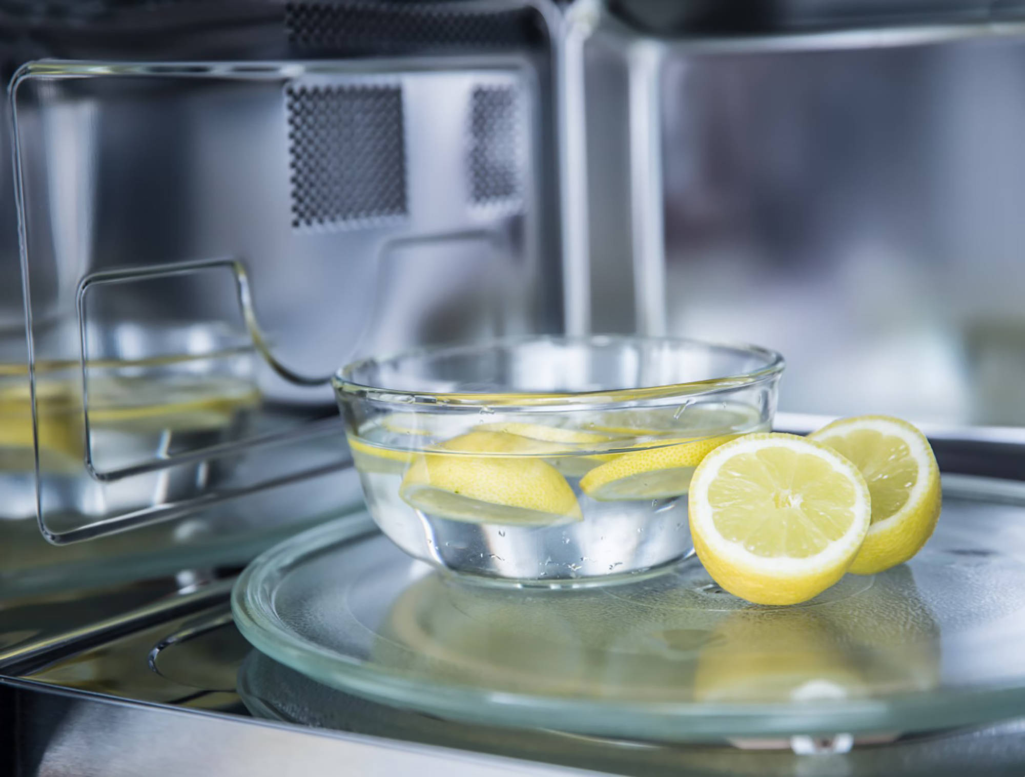 Schale mit Wasser und Zitronenscheiben auf dem Drehteller einer offenen Mikrowelle zur natürlichen Reinigung mit Dampf.