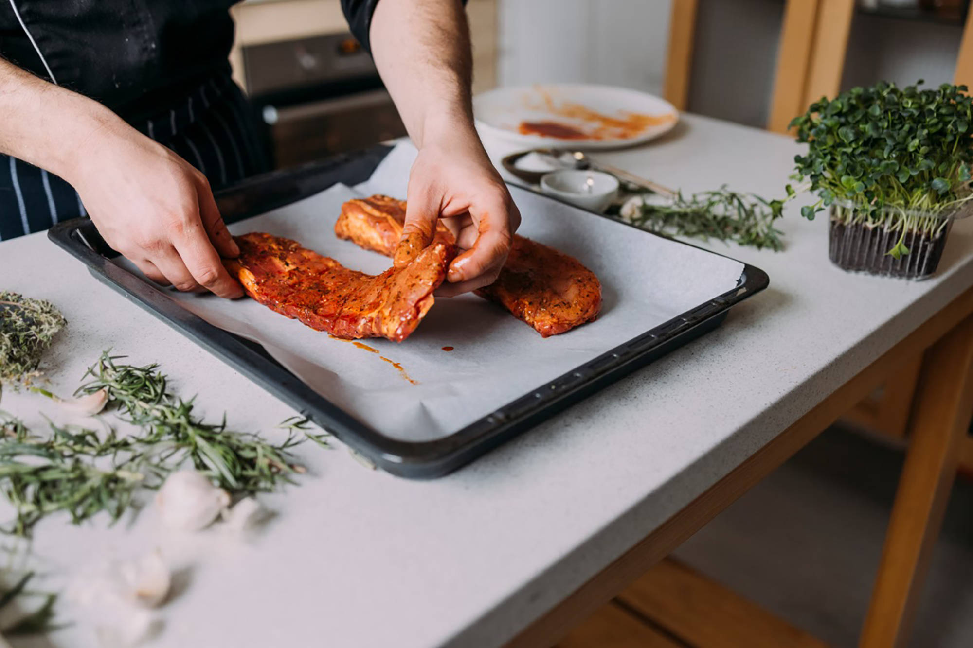 Eine person legt zwei marinierte Steaks auf ein mit Backpapier ausgelegtes Blech.