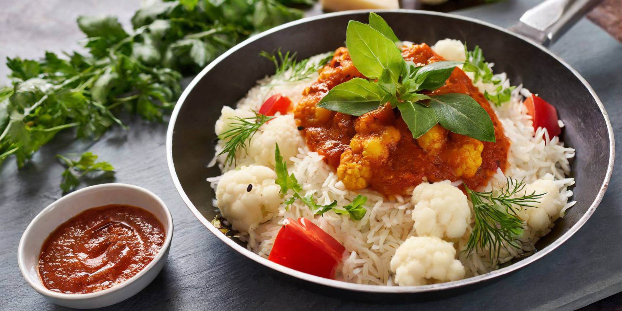 Basmatireis mit Blumenkohl-Curry und frischen Kräutern in Pfanne.