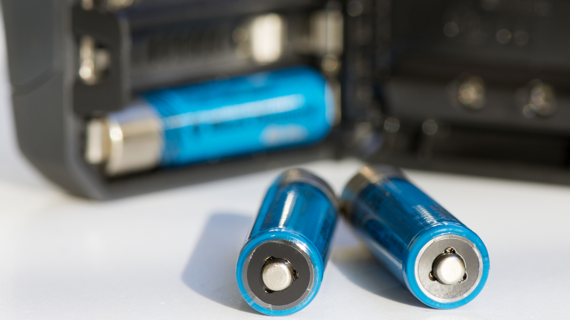 Blaue Batterien, teilweise in einem elektronischen Gerät platziert.

