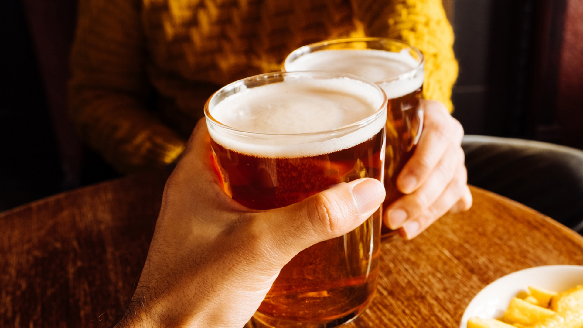 Zwei Biergläser mit Schaum werden angestoßen.