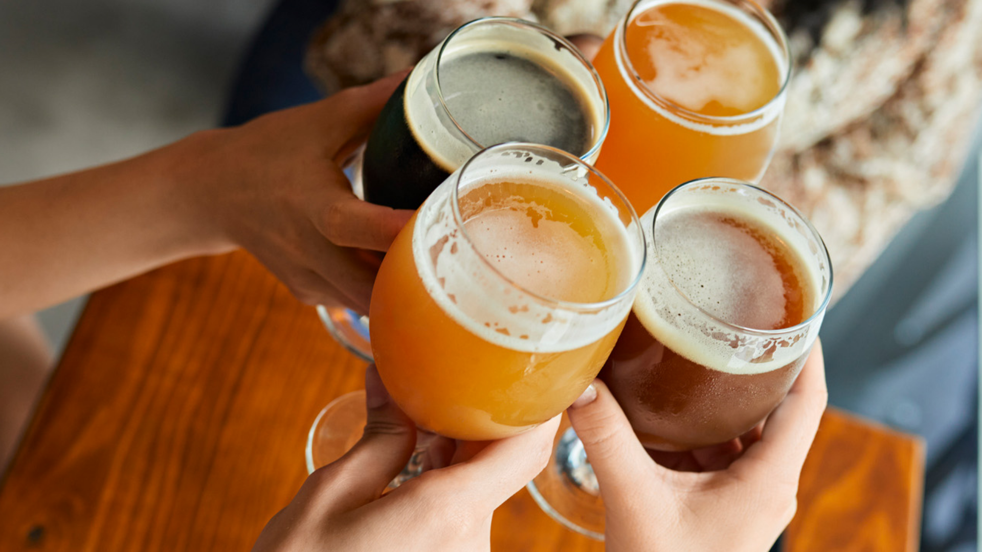 Vier Hände halten Biere unterschiedlicher Sorten hoch.
