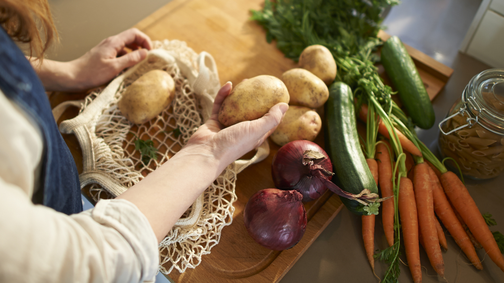Frisches Gemüse auf Holzbrett, eine Hand hält Kartoffel.