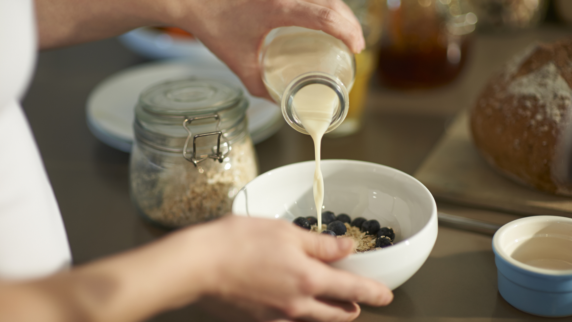 Person gießt Milch in Müsli mit Blaubeeren.