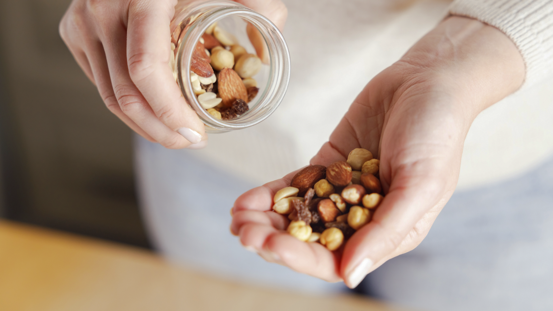 Hände gießen Nussmischung aus Glas in Hand.