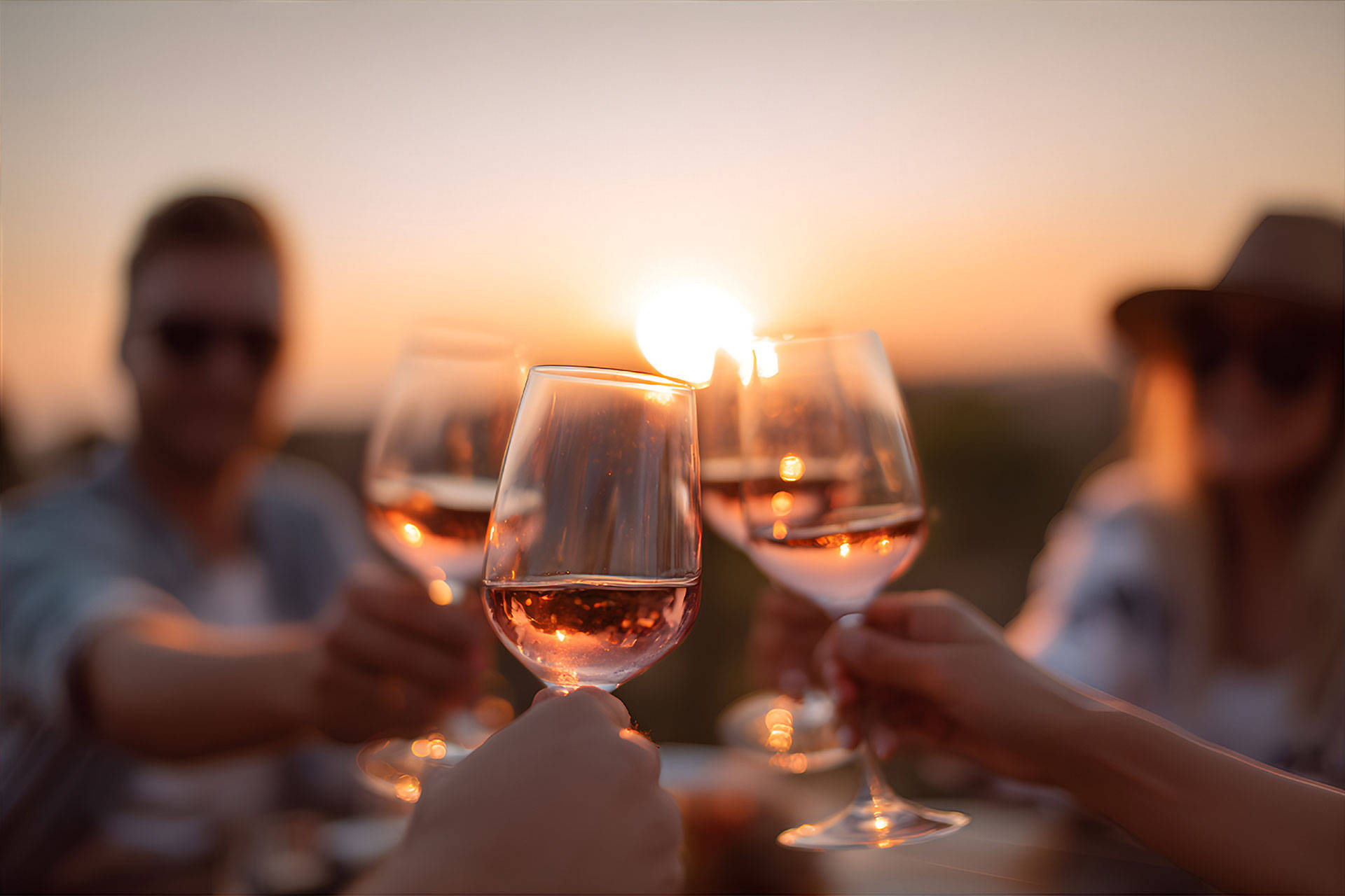 Eine Gruppe von Menschen stößt im Sonnenuntergang mit Roséwein an.