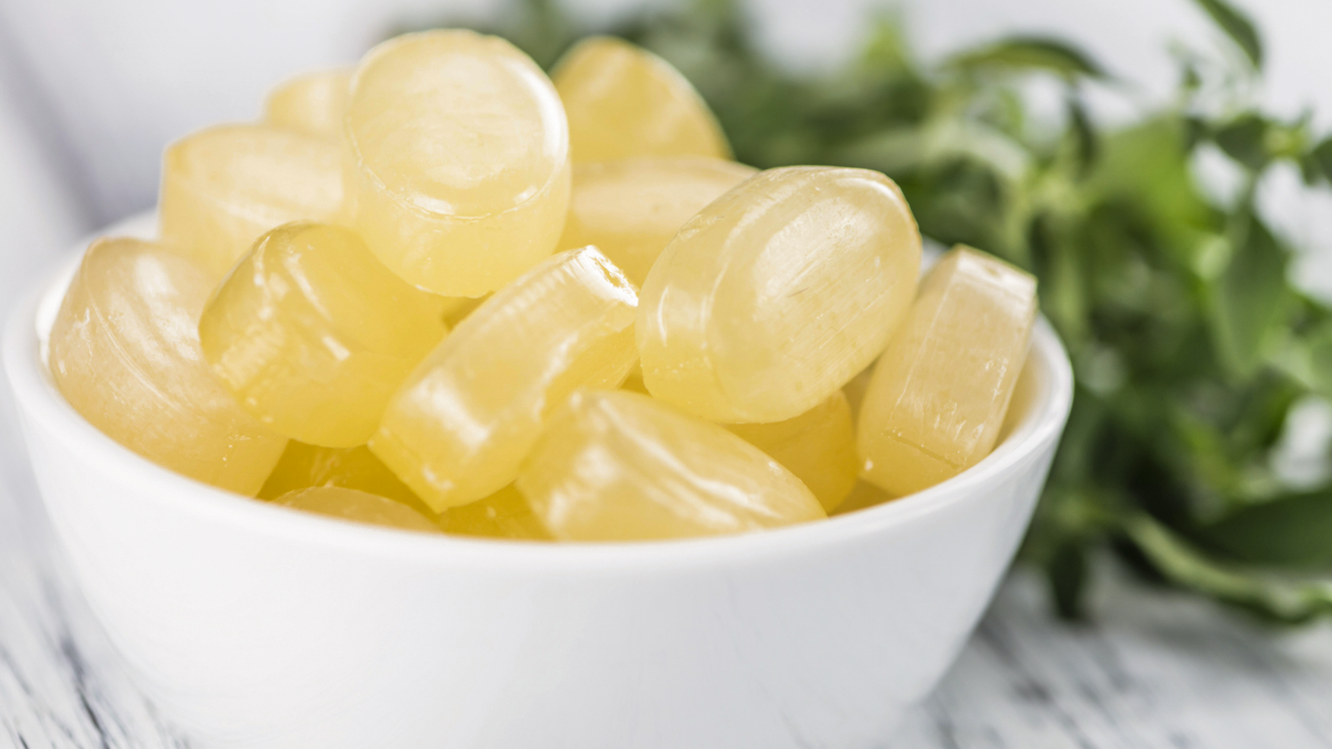 Gelbe Bonbons in einer weißen Schale mit Kräutern.