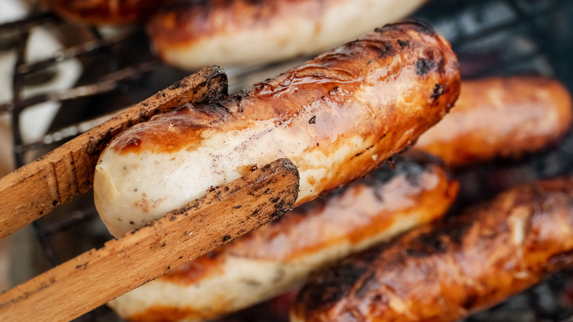 Bratwurst wird mit Grillzange auf Grillrost gewendet.