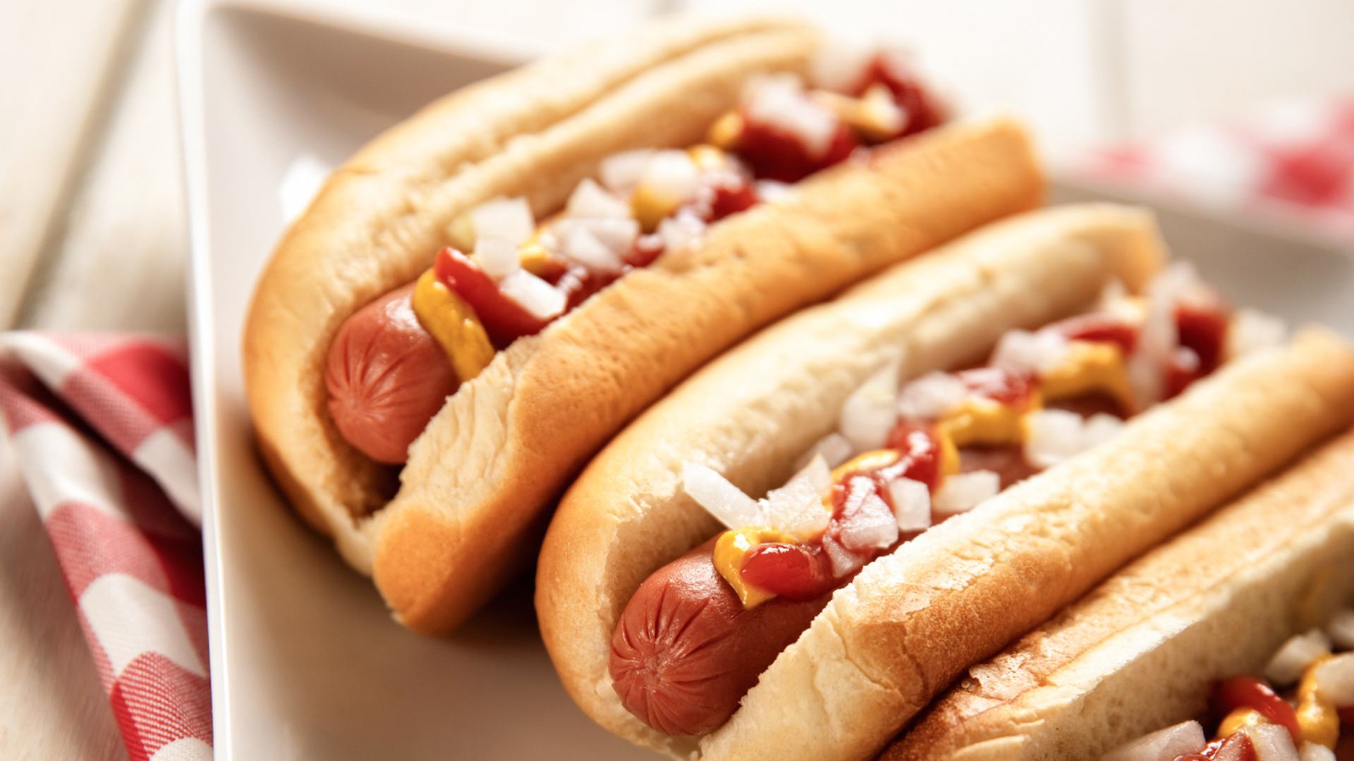 Zwei Hot Dogs mit Senf, Ketchup und Zwiebeln auf Teller.