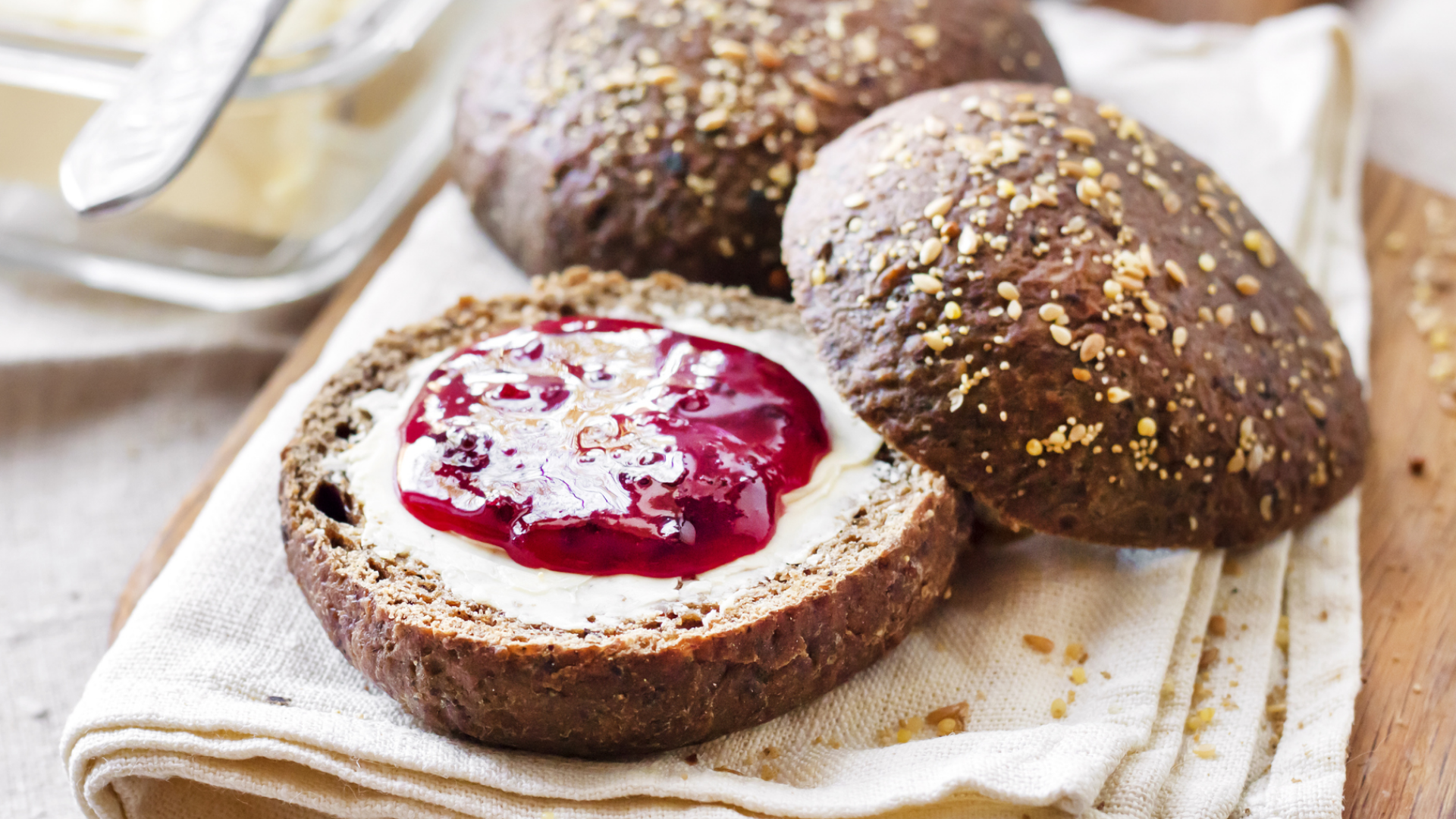 Dunkle Körnerbrötchen mit Butter und Marmelade.