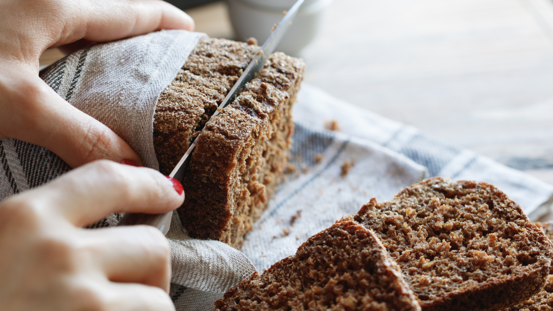 Hände schneiden dunkles Vollkornbrot in Scheiben.