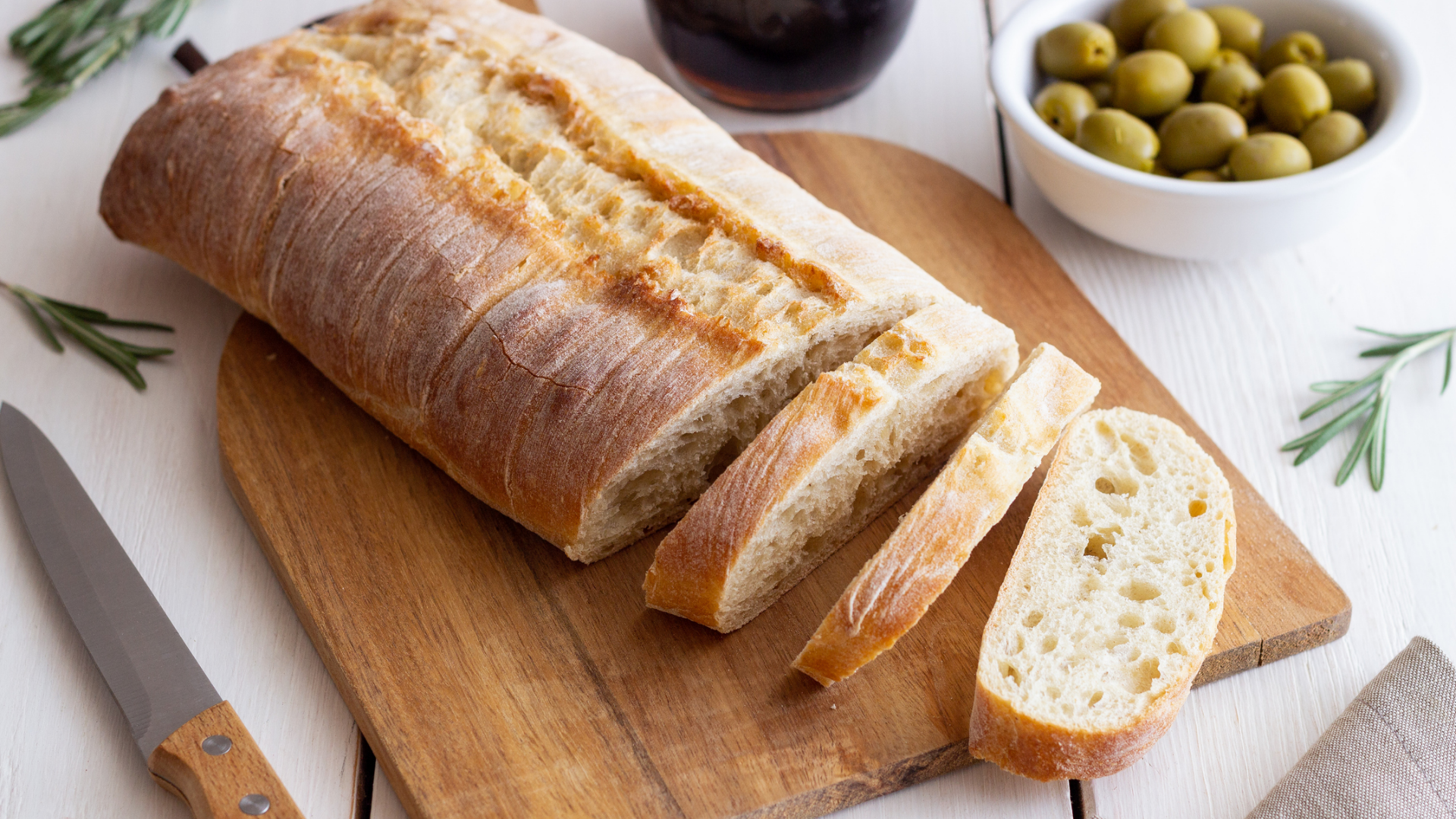 Geschnittenes Brot auf Schneidebrett mit Oliven und Rosmarinzweigen.