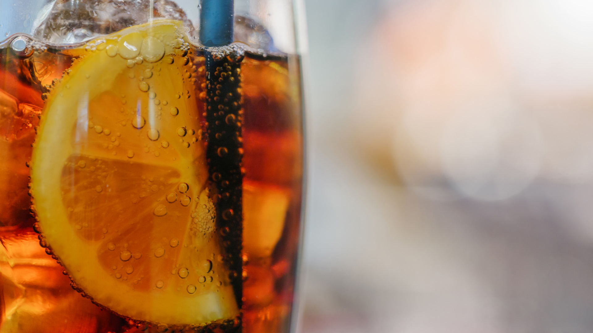 Kalter Drink mit Eis, Zitrone und blauem Strohhalm.