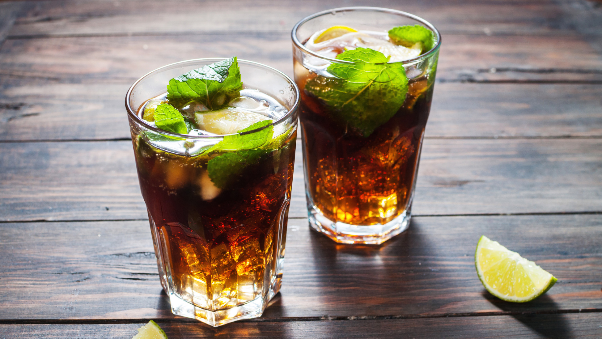 Zwei Cola-Getränke mit Limette und Minze auf Holzoberfläche.