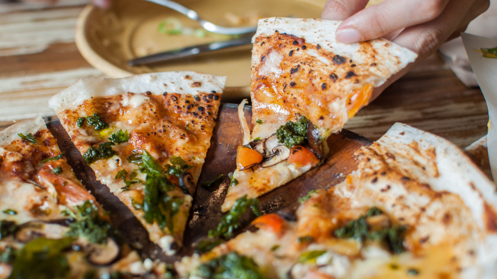 Pizza mit Gemüse und Pesto wird von Hand genommen.