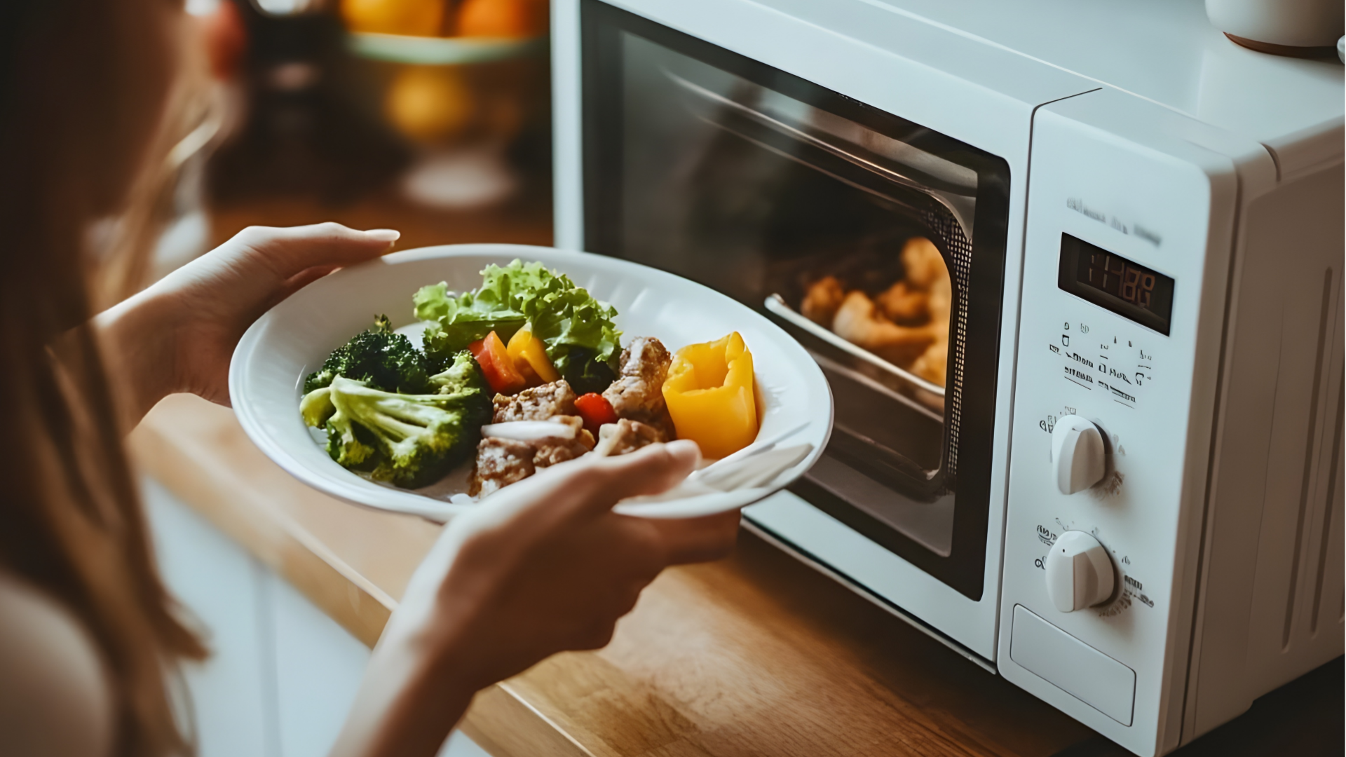 Frau hält Teller mit Essen vor Mikrowelle.