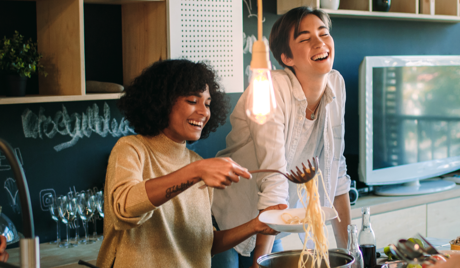 Zwei lachende Frauen servieren Nudeln in der Küche.
