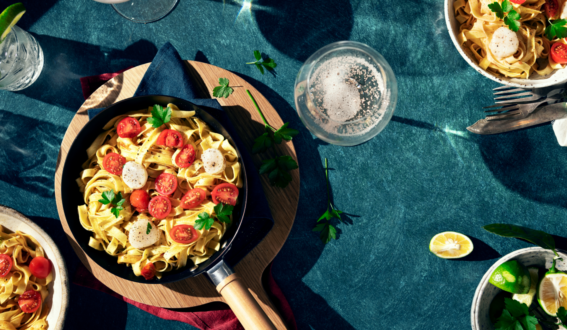 Nudelgerichte mit Tomaten, Mozzarella, Petersilie in Pfanne und Schalen.