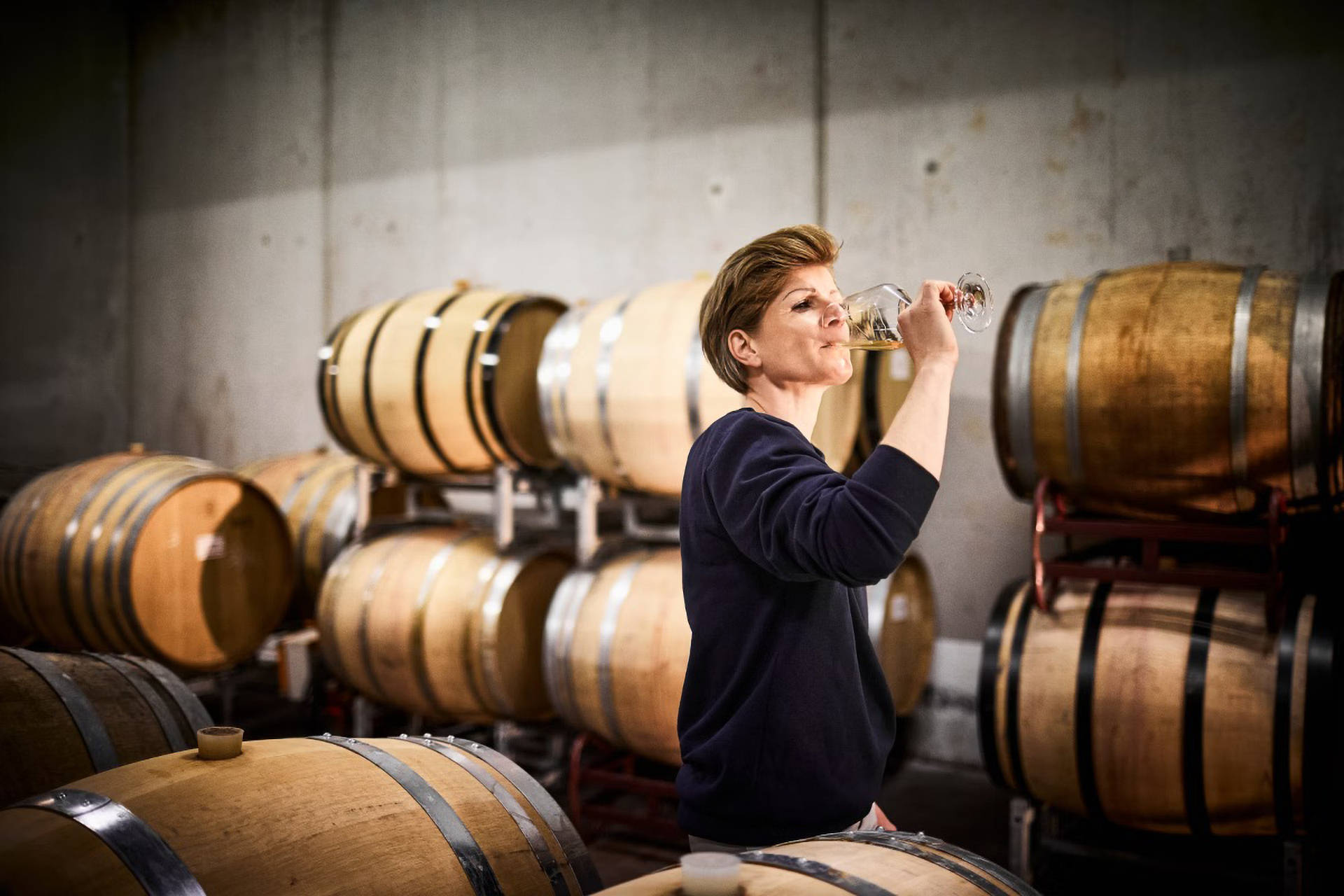 Die Winzerin probiert einen Cuvée Weißwein in der Kellnerei, umgeben von Eichenfässern.