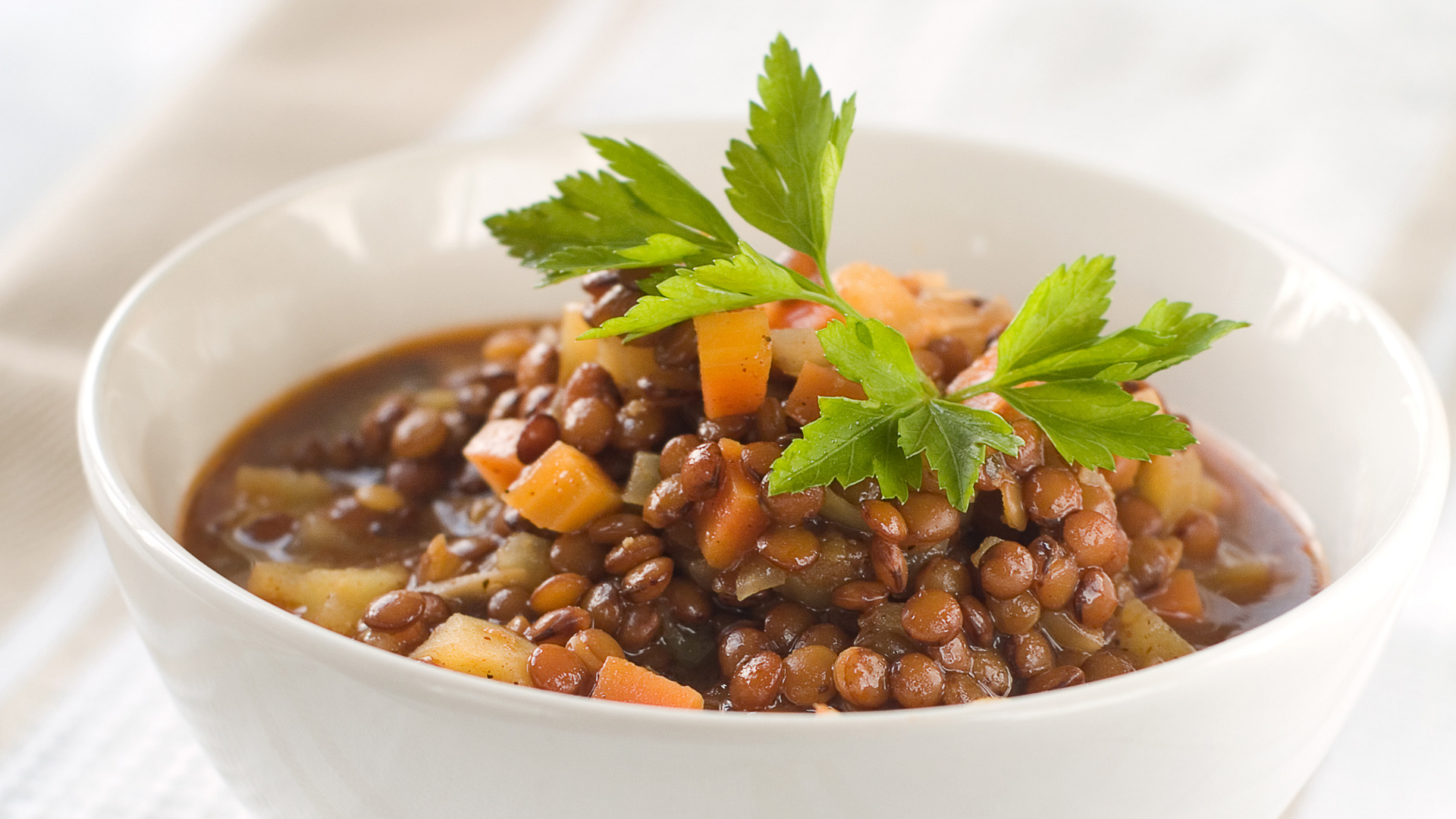 Linseneintopf mit Karotten, Kartoffeln und Petersilie in weißer Schale.