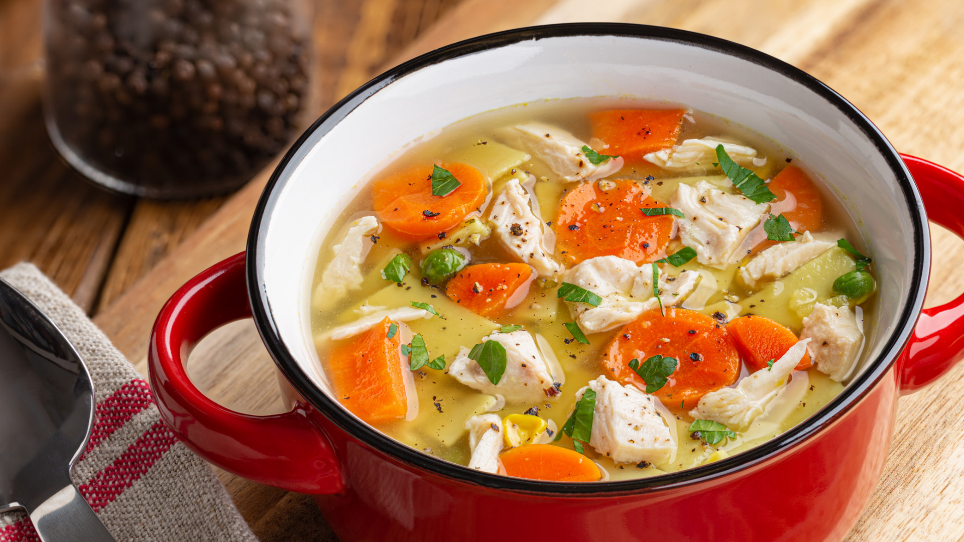 Hühnersuppe mit Gemüse in rotem Topf auf Holz.