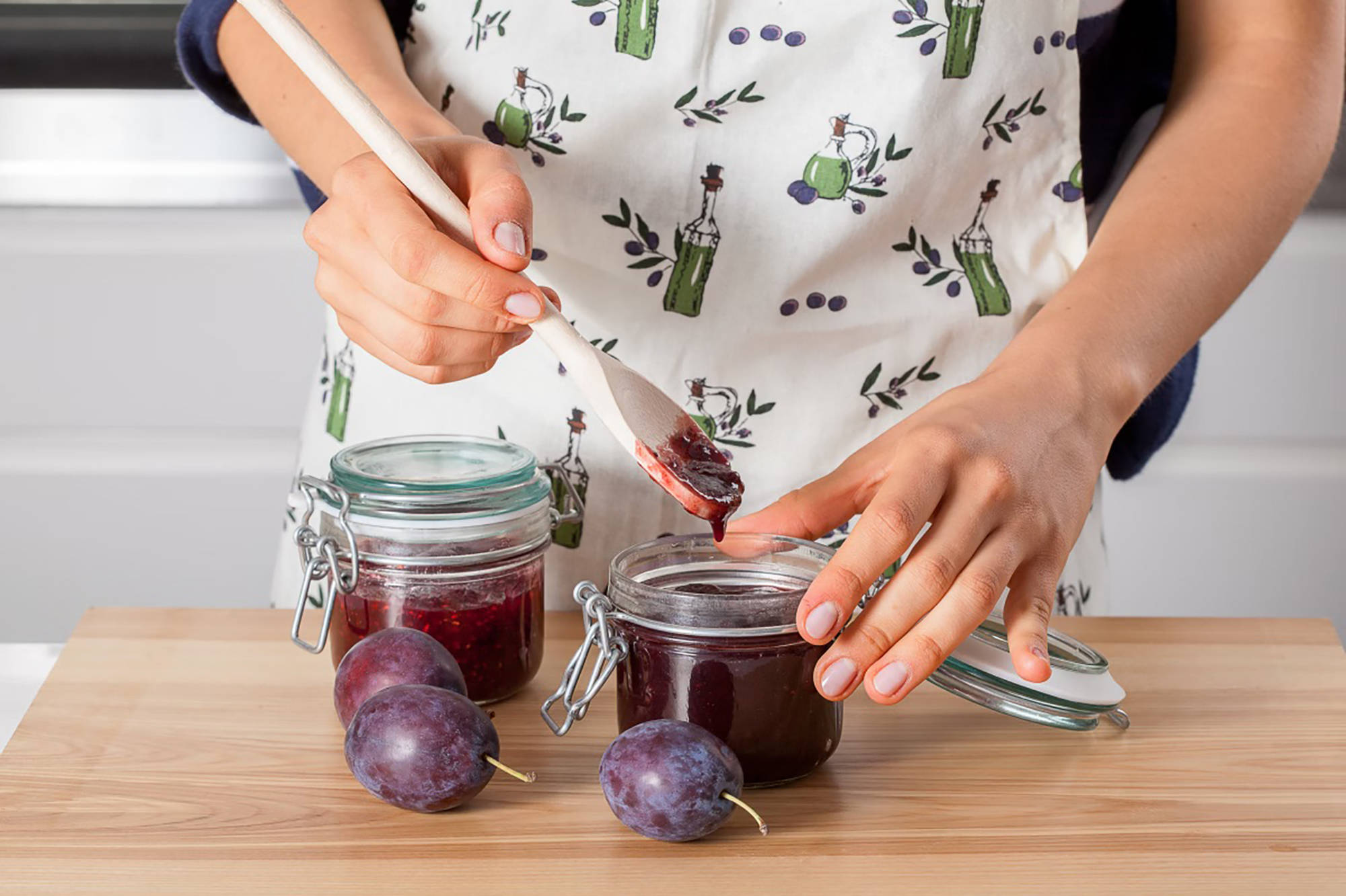 Person verschließt ein Glas mit Pflaumenmarmelade nach dem Einkochen im Backofen.