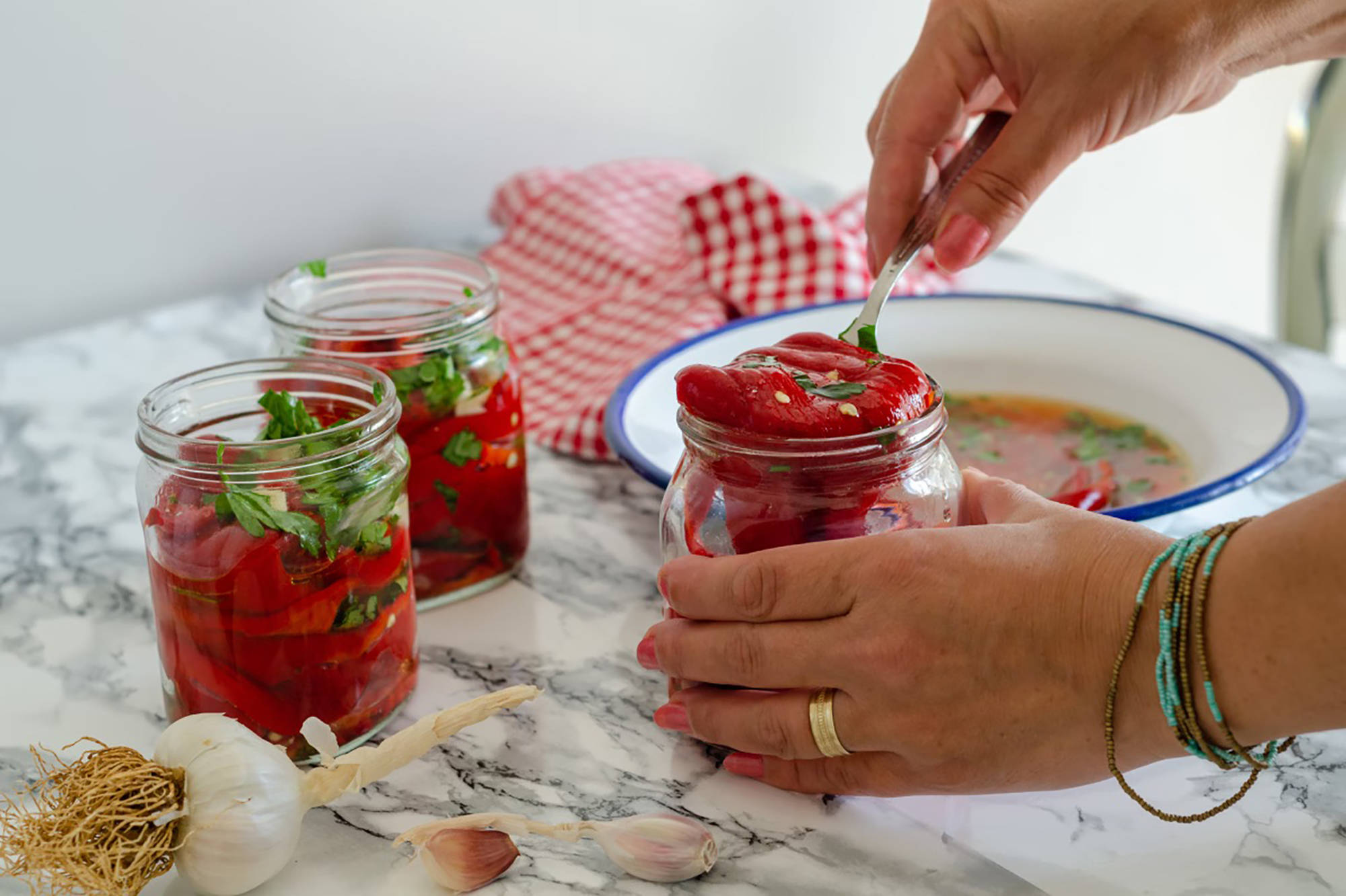 Person füllt marinierte Paprika mit Kräutern in ein Glas zur Verarbeitung für das Einkochen im Backofen.