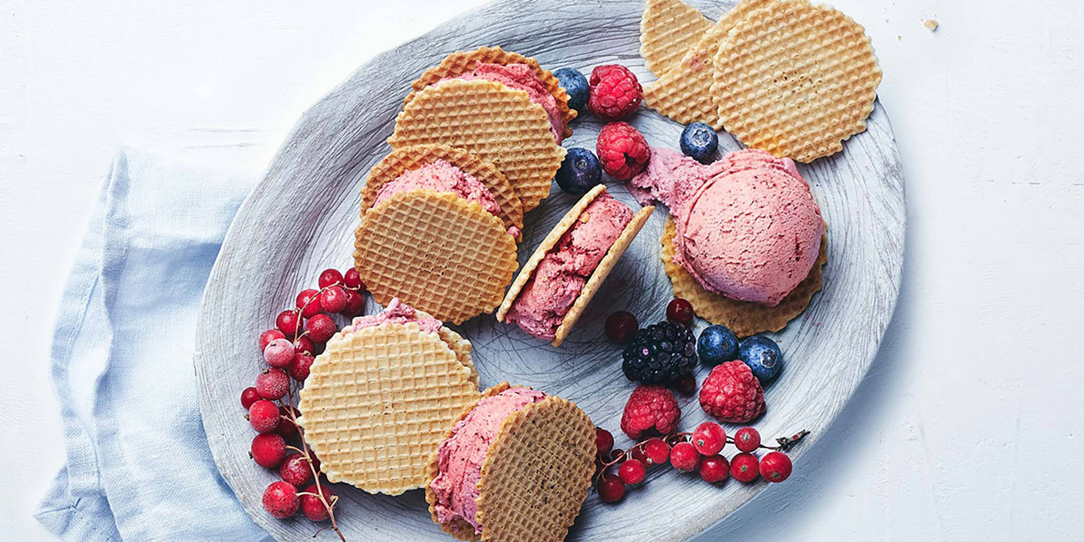Fruchteis-Sandwiches, Kugel Eis und Beeren auf Holzplatte.