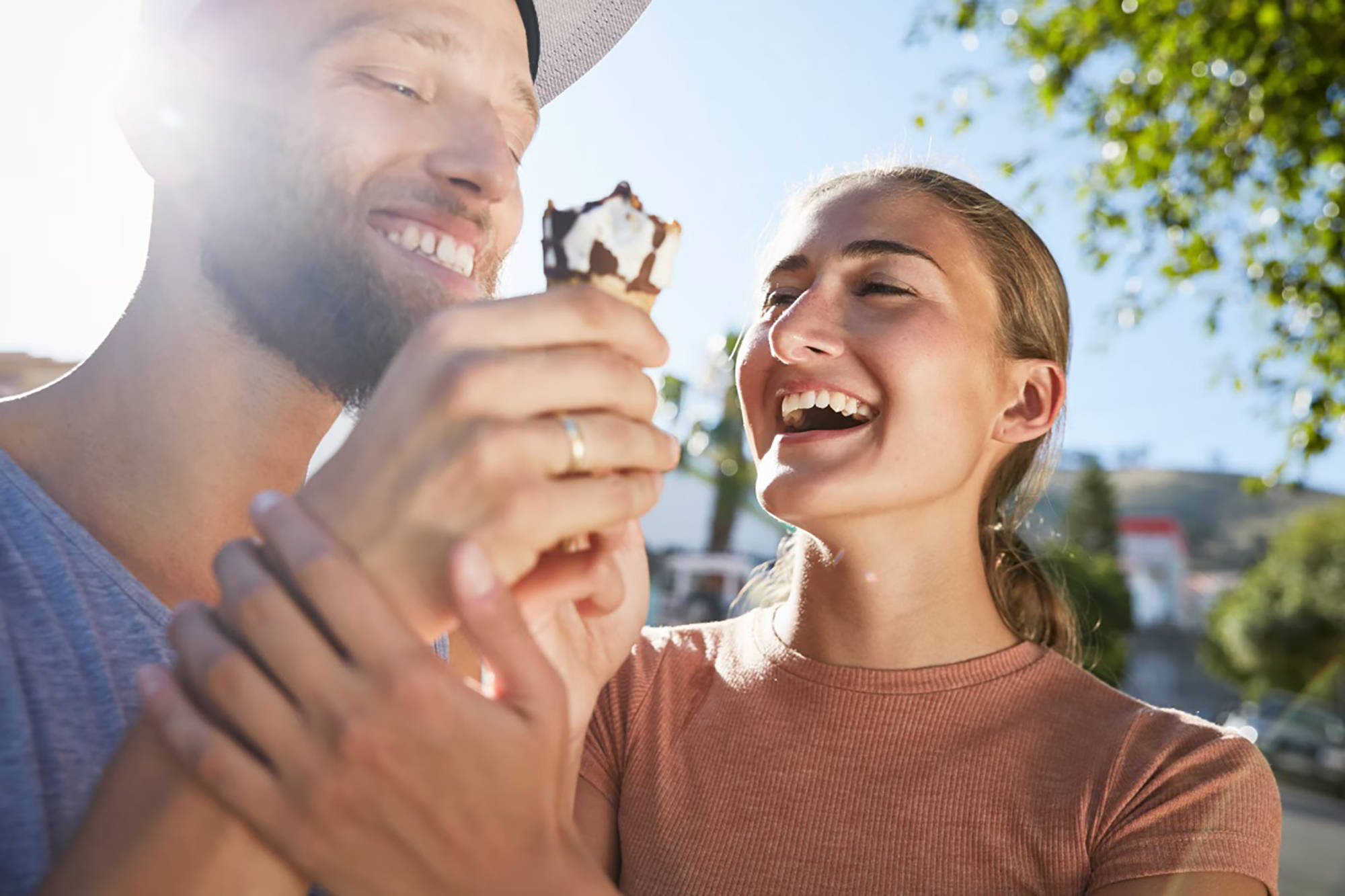 Lachendes Paar teilt sich ein Hörnchen-Eis bei Sonnenschein.