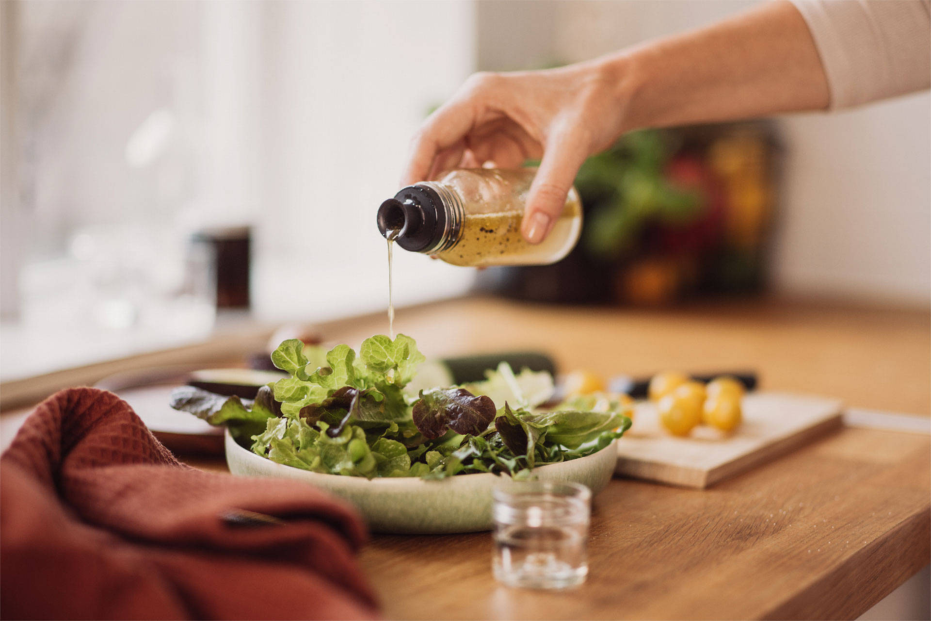 Eine Person gießt Vinaigrette aus einer Flasche über frischen grünen Salat in einer Schale auf einem Holztisch.