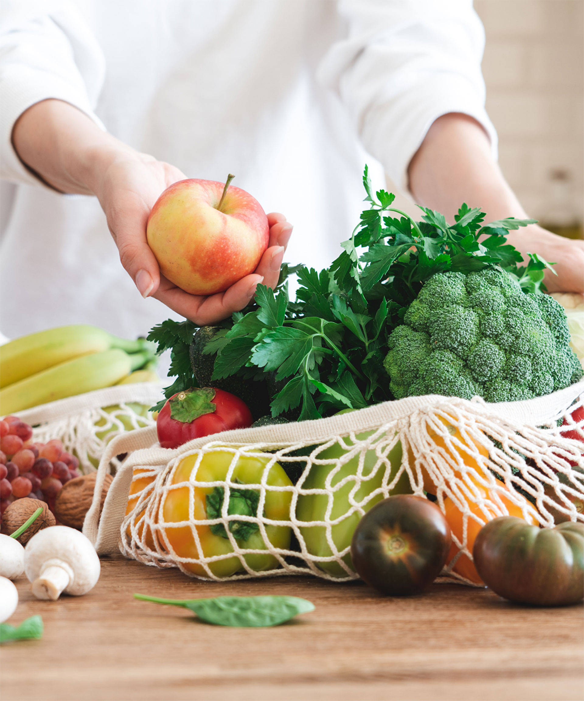 Person holt einen Apfel aus einer großen Netz-Einkaufstasche, die gefüllt ist mit viel frischem Gemüse.
