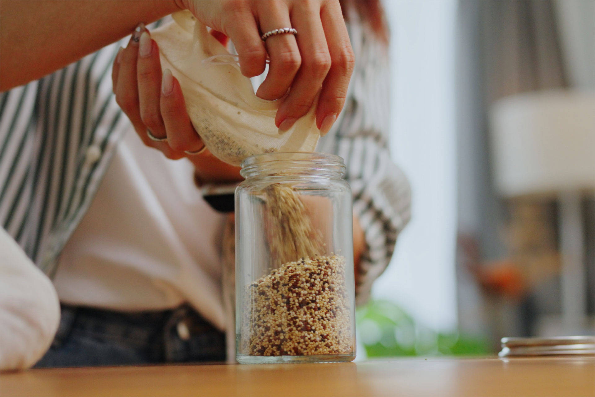 Nahaufnahme einer Person, die Quinoa aus einem Stoffbeutel in ein Glasgefäß füllt.