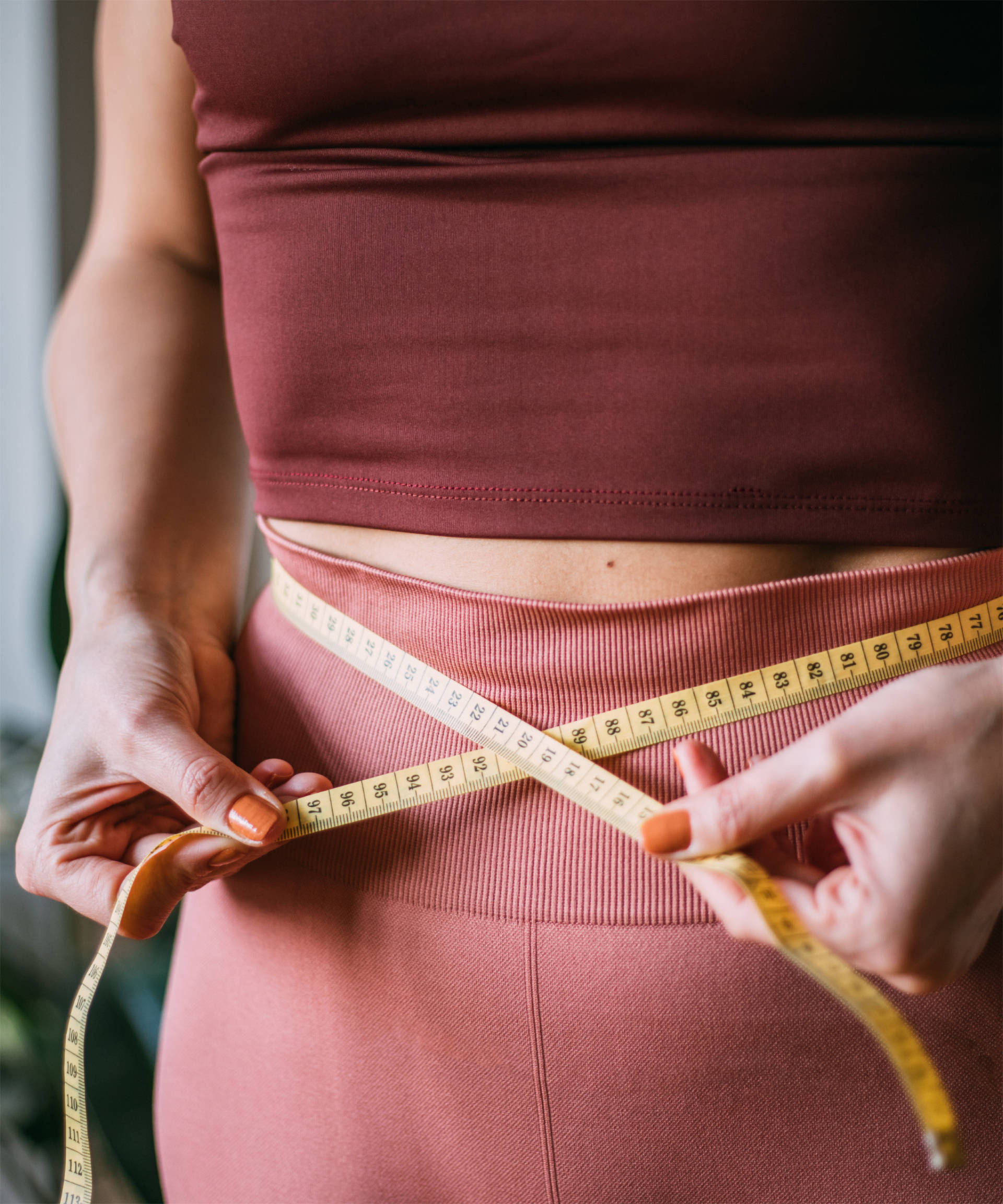 Frau in Sportkleidung misst mit einem Maßband ihren Taillenumfang.