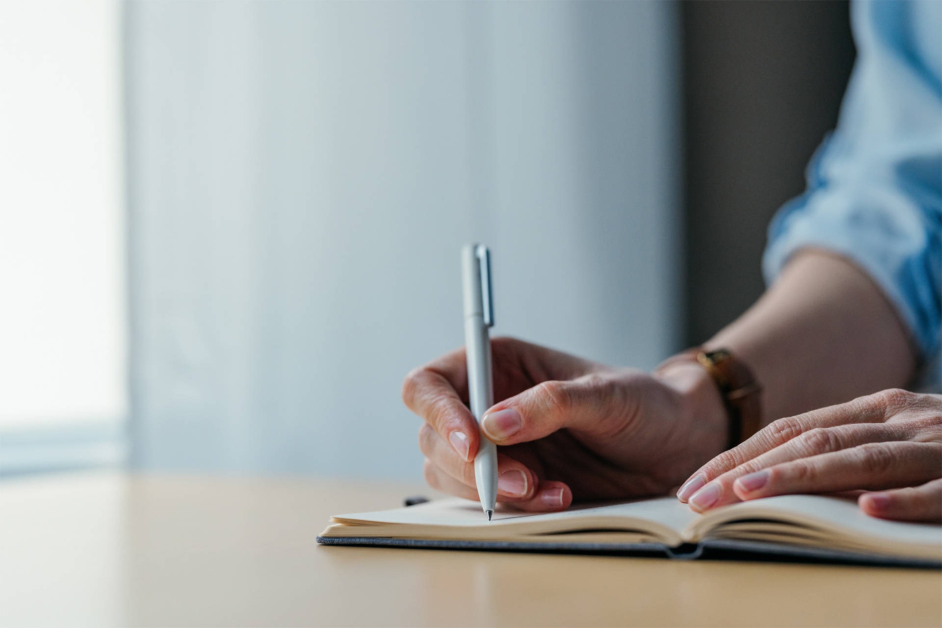 Person schreibt mit einem Kugelschreibe in ein Notizbuch.