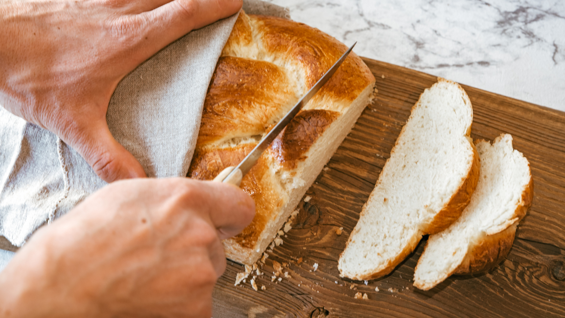 Person schneidet geflochtenes Brot auf Holzbrett.