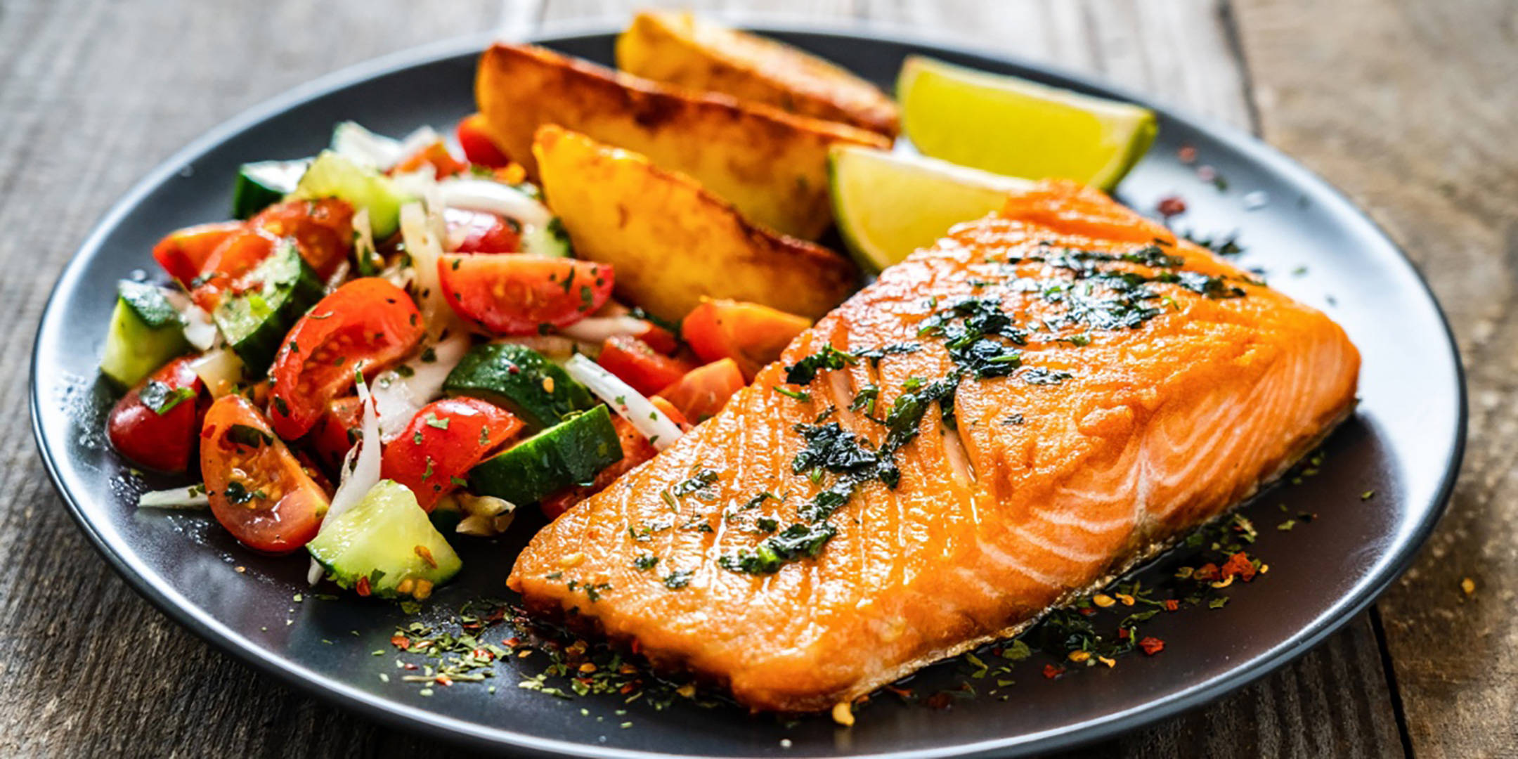 Gebratenes Lachsfilet mit Kartoffelspalten, Salat und Limette.